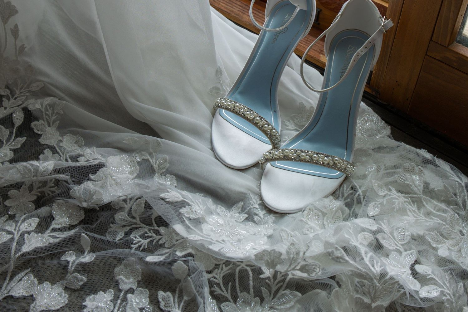 Light blue wedding heels with rhinestone details rest elegantly on delicate white lace fabric.