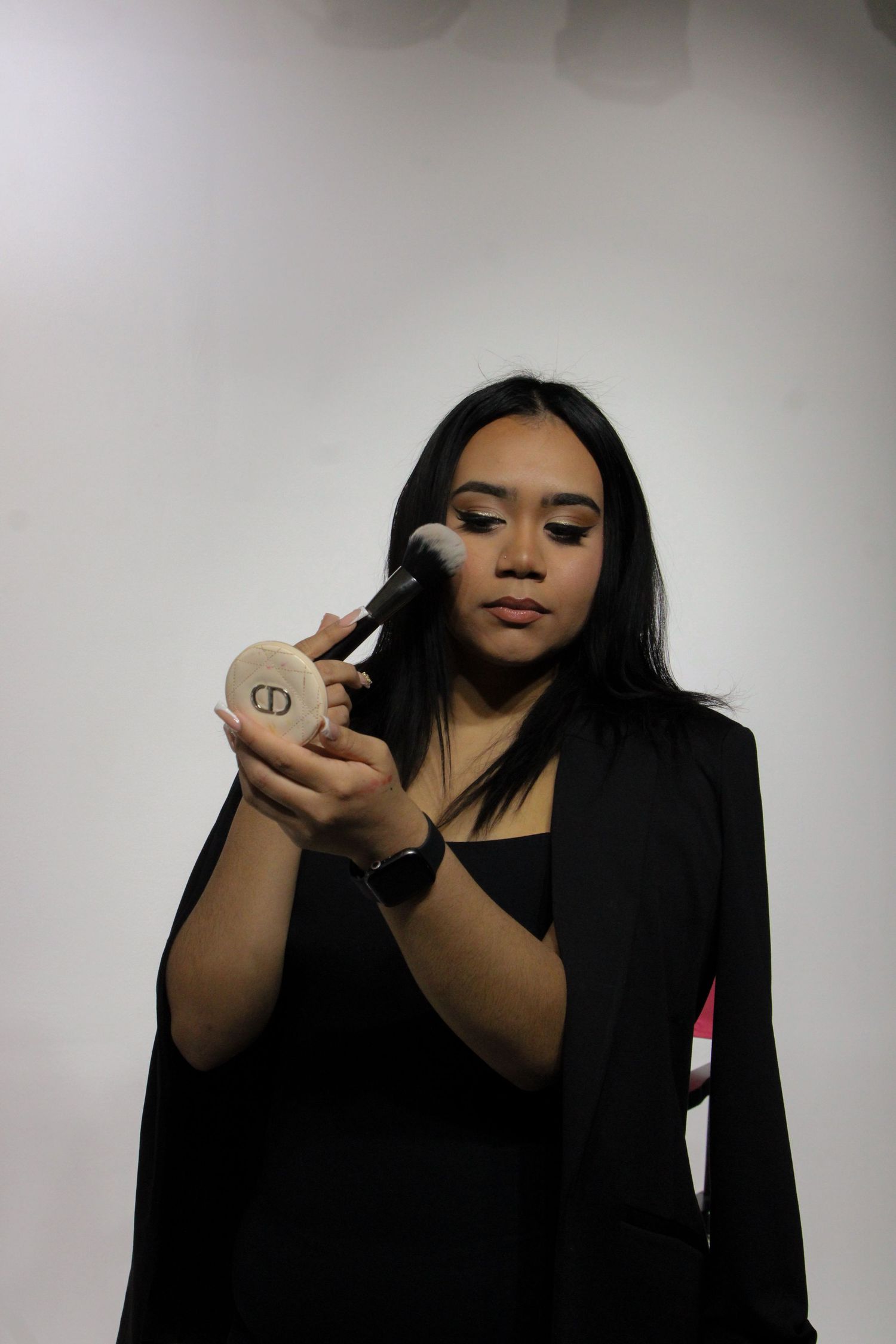 A person in a black top demonstrates applying makeup while showing different angles against a light background.