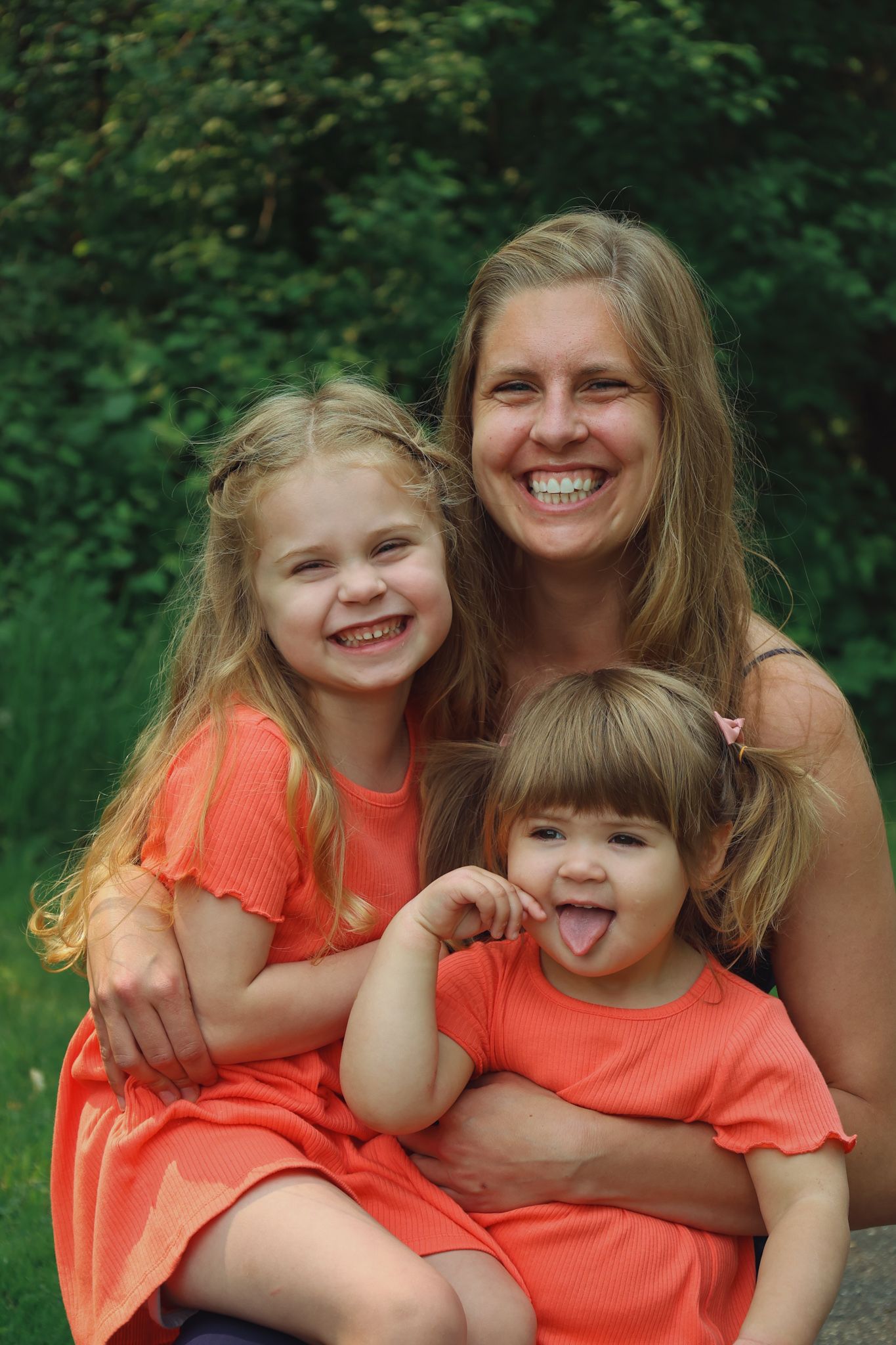 A joyful family moment outdoors with matching coral dresses sitting together against a green background.