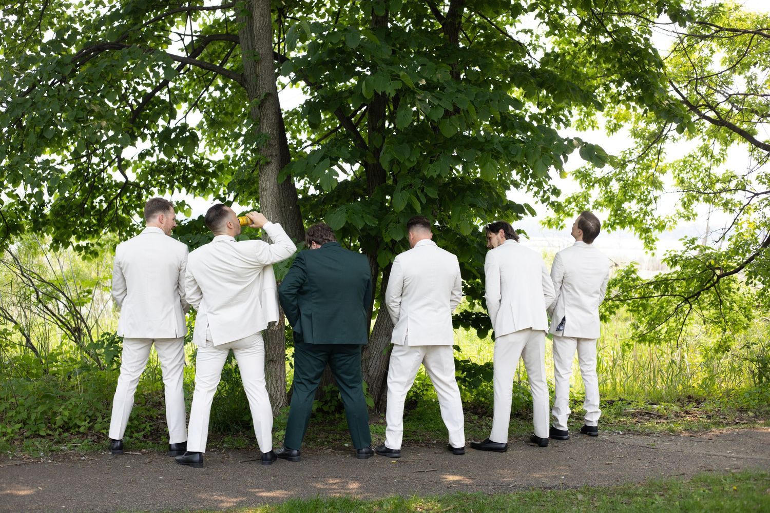 A group wearing coordinated white outfits walks away into a scenic wooded outdoor path while spending time together.
