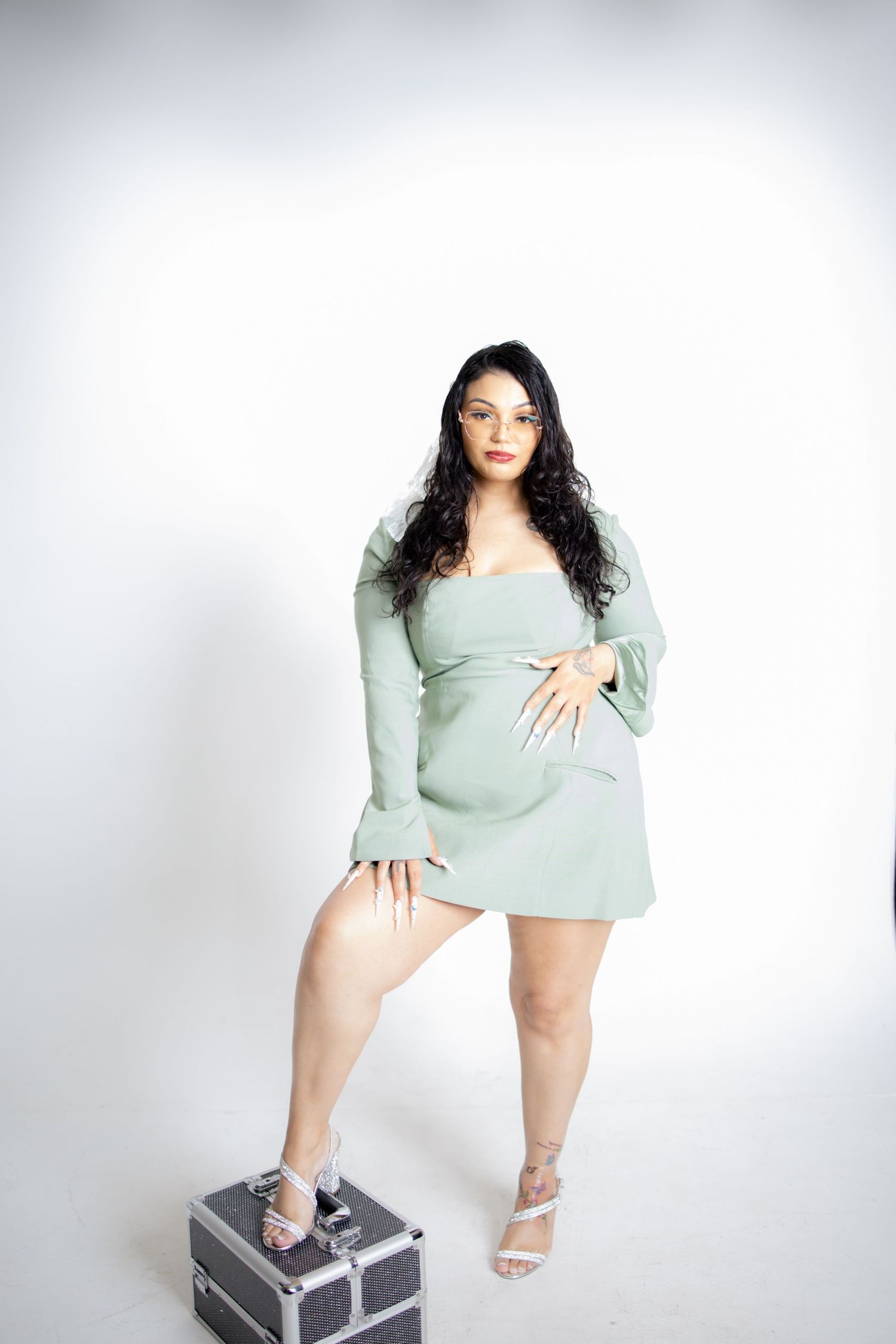 Figure in a mint green outfit poses elegantly against white backdrop with a travel case prop.