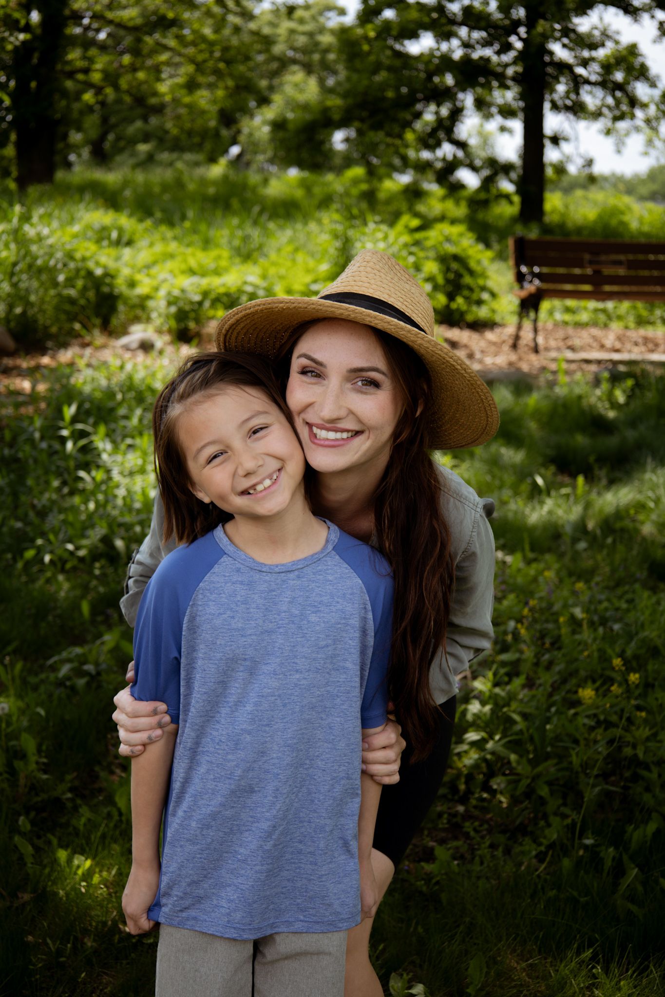 A loving embrace captured outdoors in a lush green garden with a wooden bench visible in the background.
