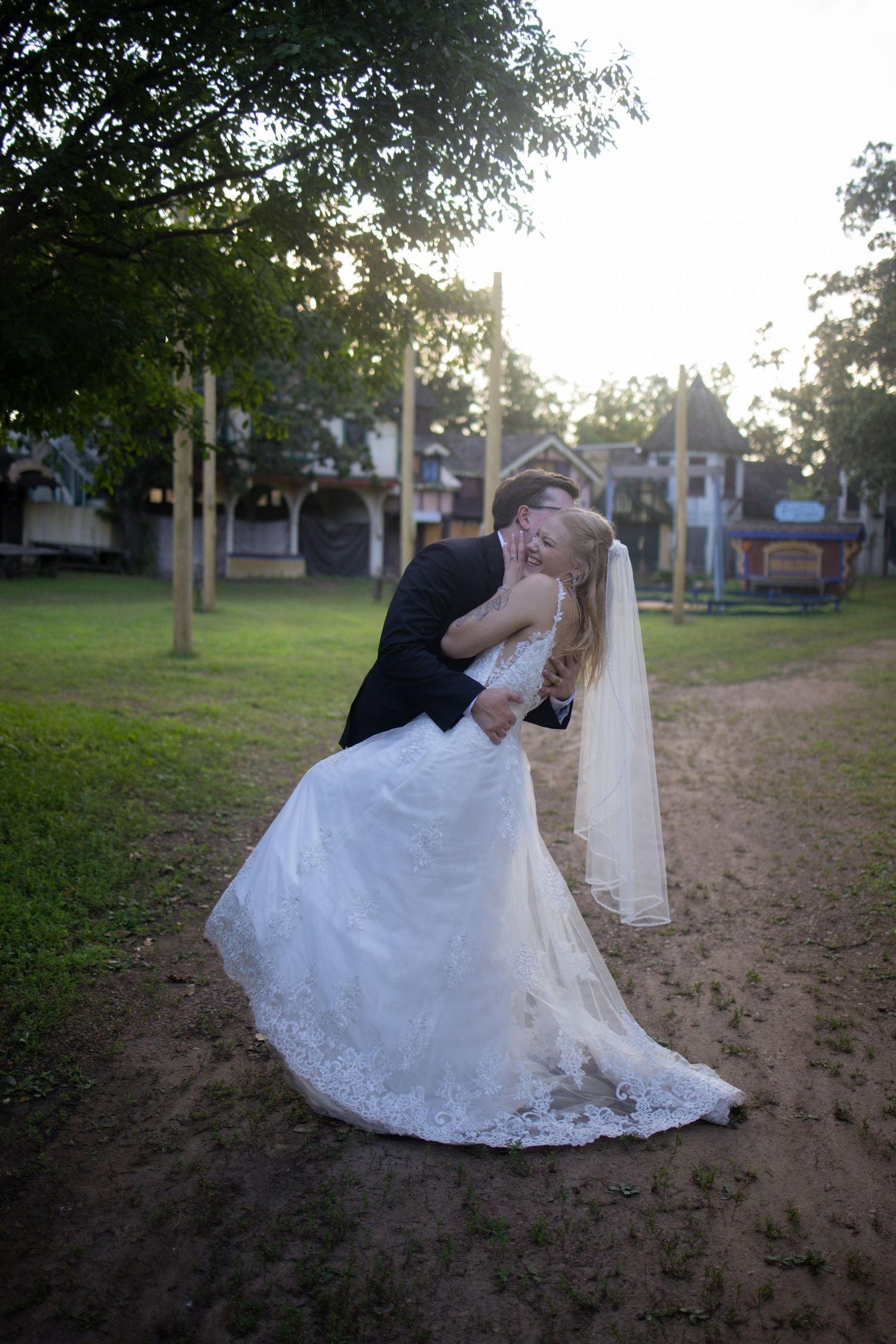 A couple in wedding attire share a romantic dip pose during their outdoor photo session at sunset in a park.