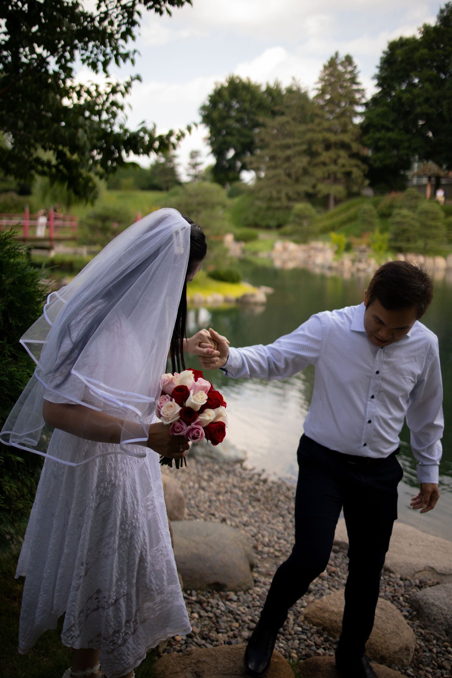 Newlywed couple playfully poses by a scenic lake with flowing veil and red rose bouquet in a sequence of candid shots.