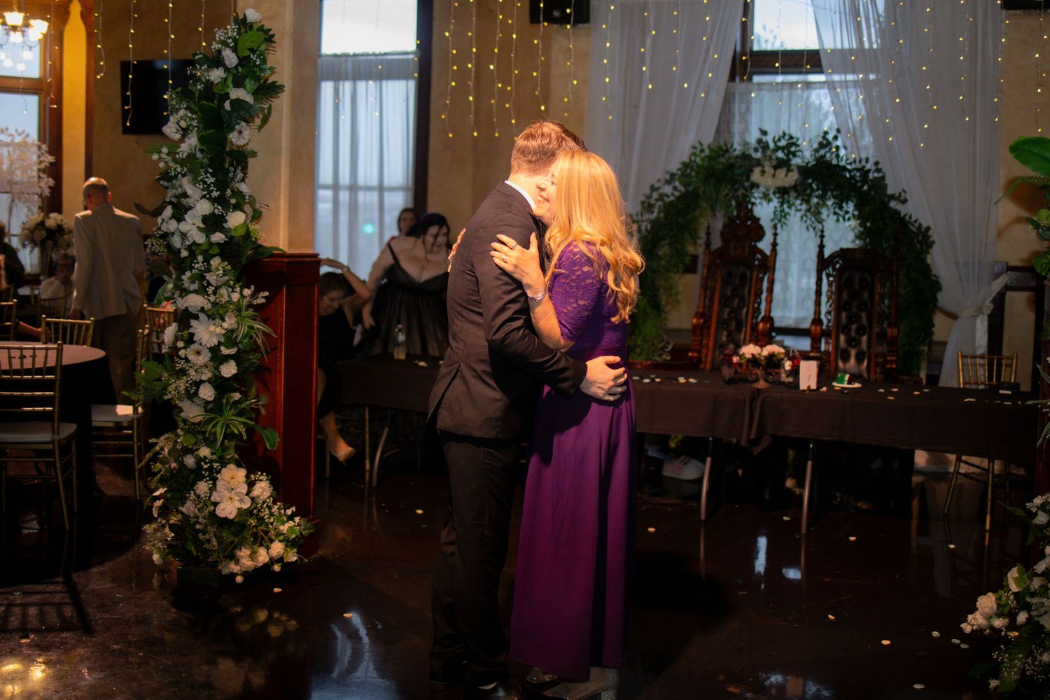 People dancing and celebrating at an elegant wedding reception decorated with floral arrangements and soft lighting.