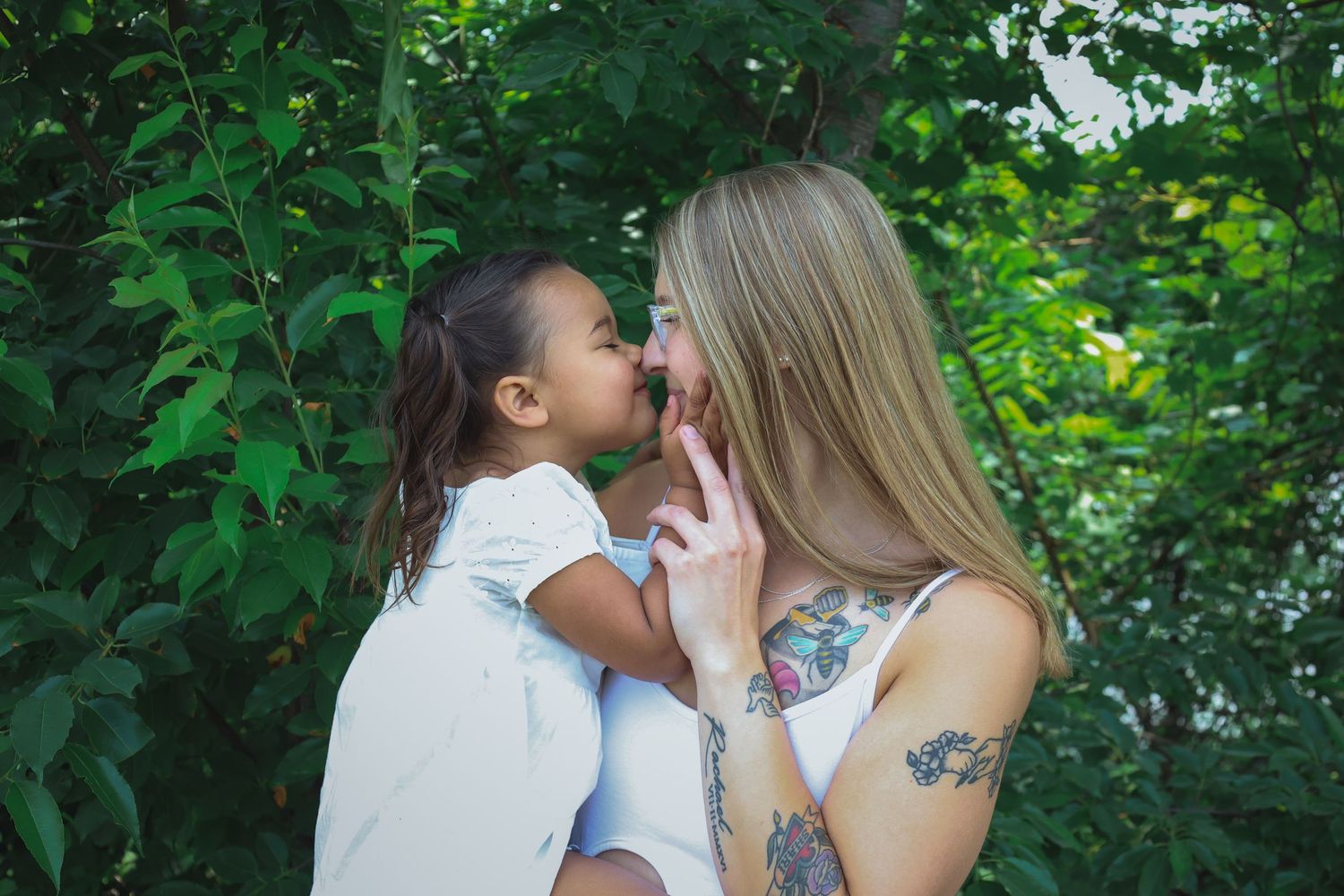 A romantic couple embraces tenderly while surrounded by lush green foliage in a natural outdoor setting.