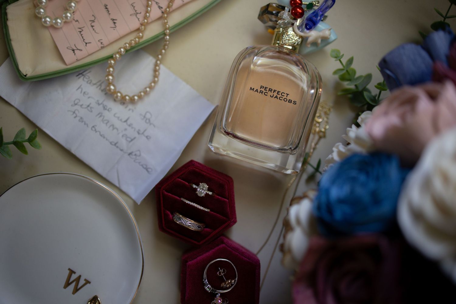 Wedding details including invitations, jewelry, perfume bottles and delicate decor arranged on a light surface.