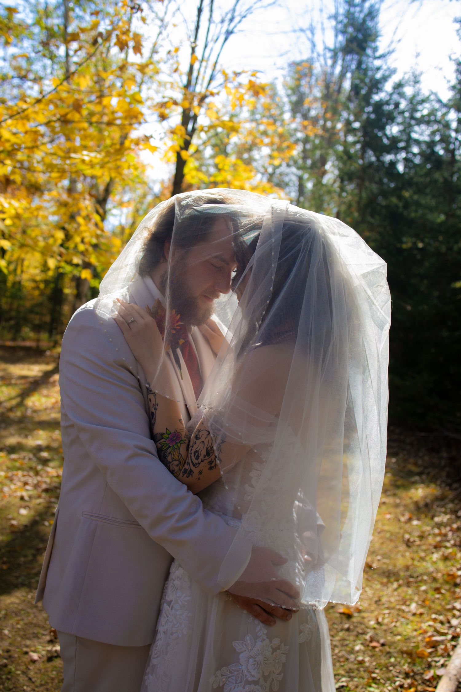 A couple shares a romantic kiss under golden autumn foliage in a sunlit outdoor setting.