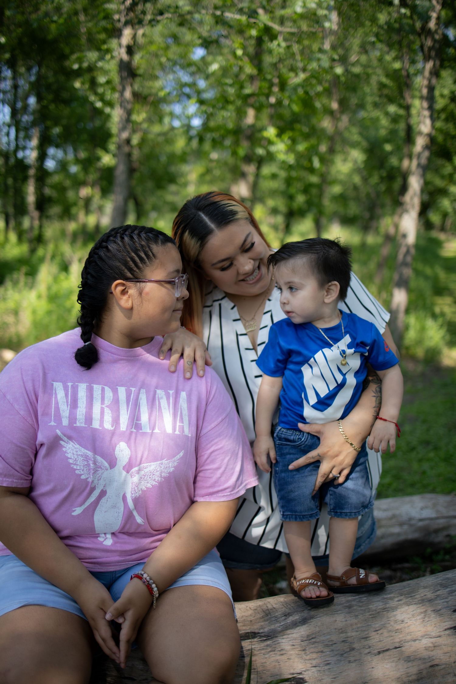 Candid family photos of mother and young child sitting together on a log in a lush green forest setting.