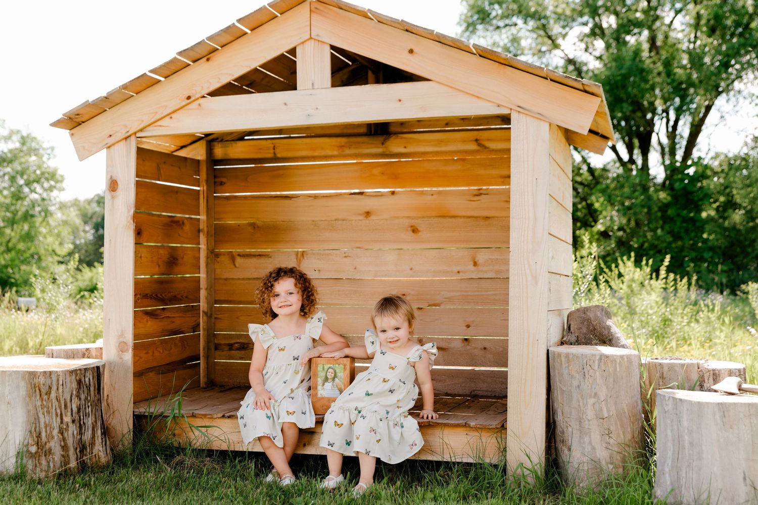 Rustic wooden playhouse in backyard surrounded by trees and greenery during summer day.