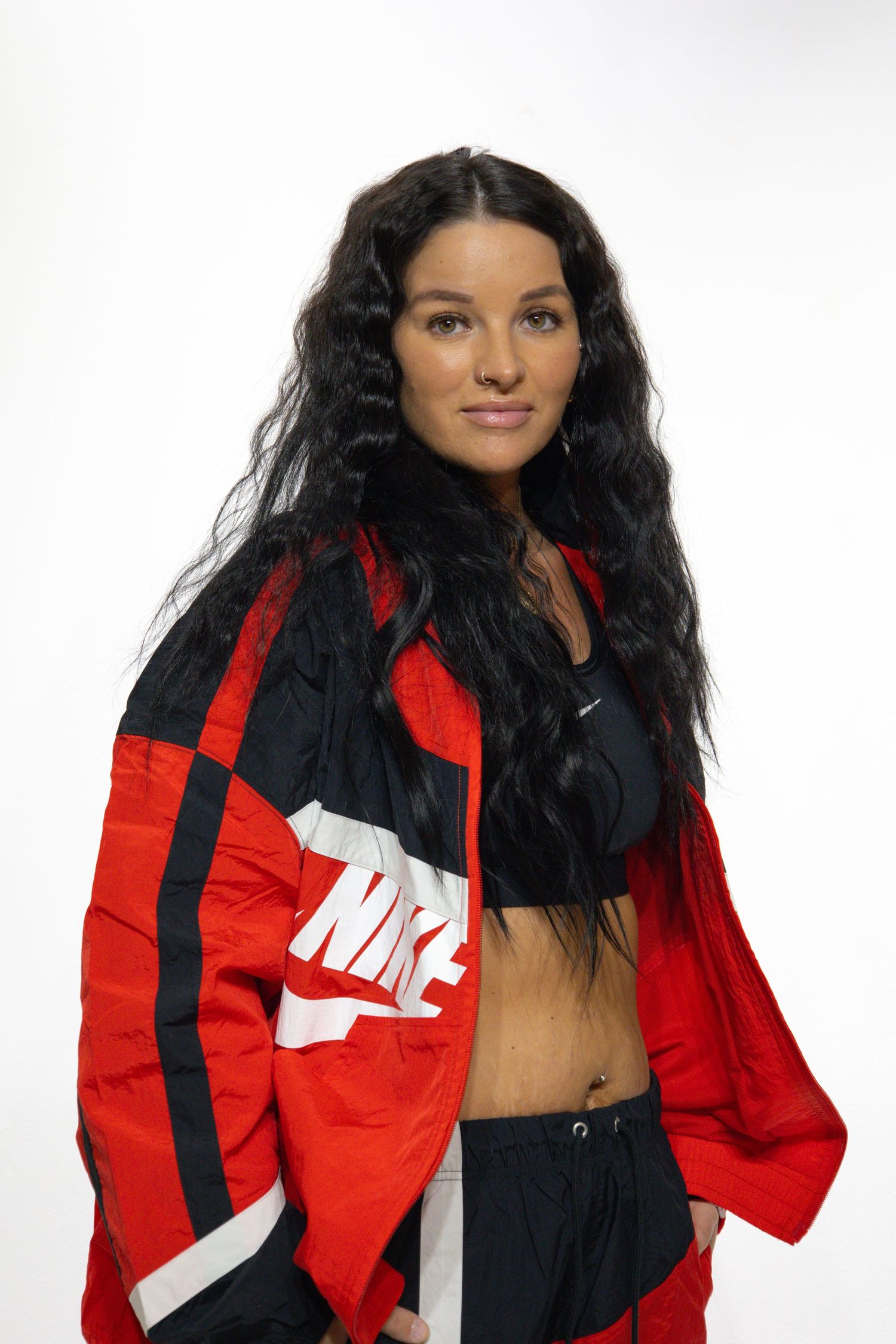 A person wearing a red and black Nike windbreaker jacket poses against a white background.