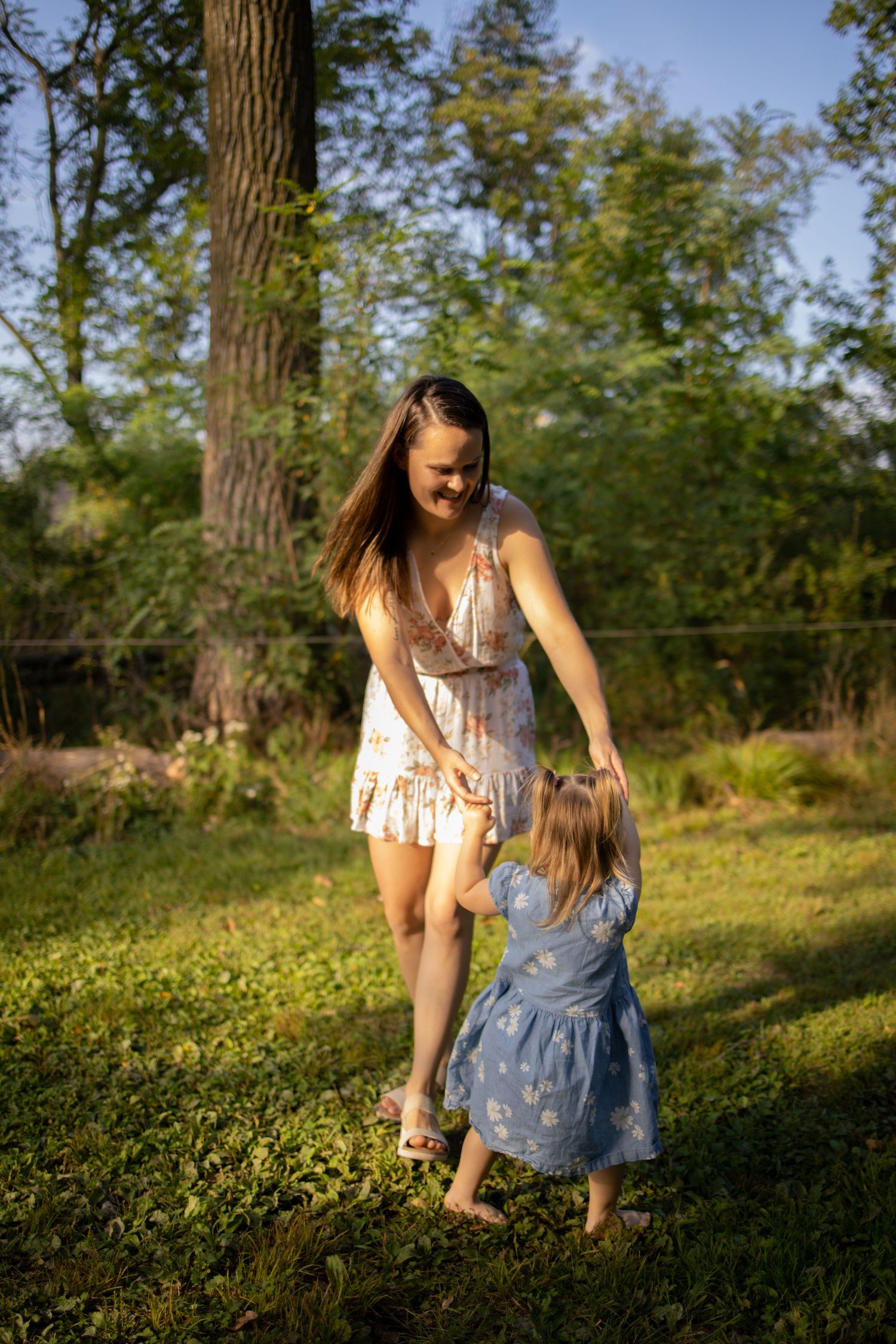 Figure in a blue dress bends down to pick wildflowers in a sunny meadow on a warm summer afternoon.