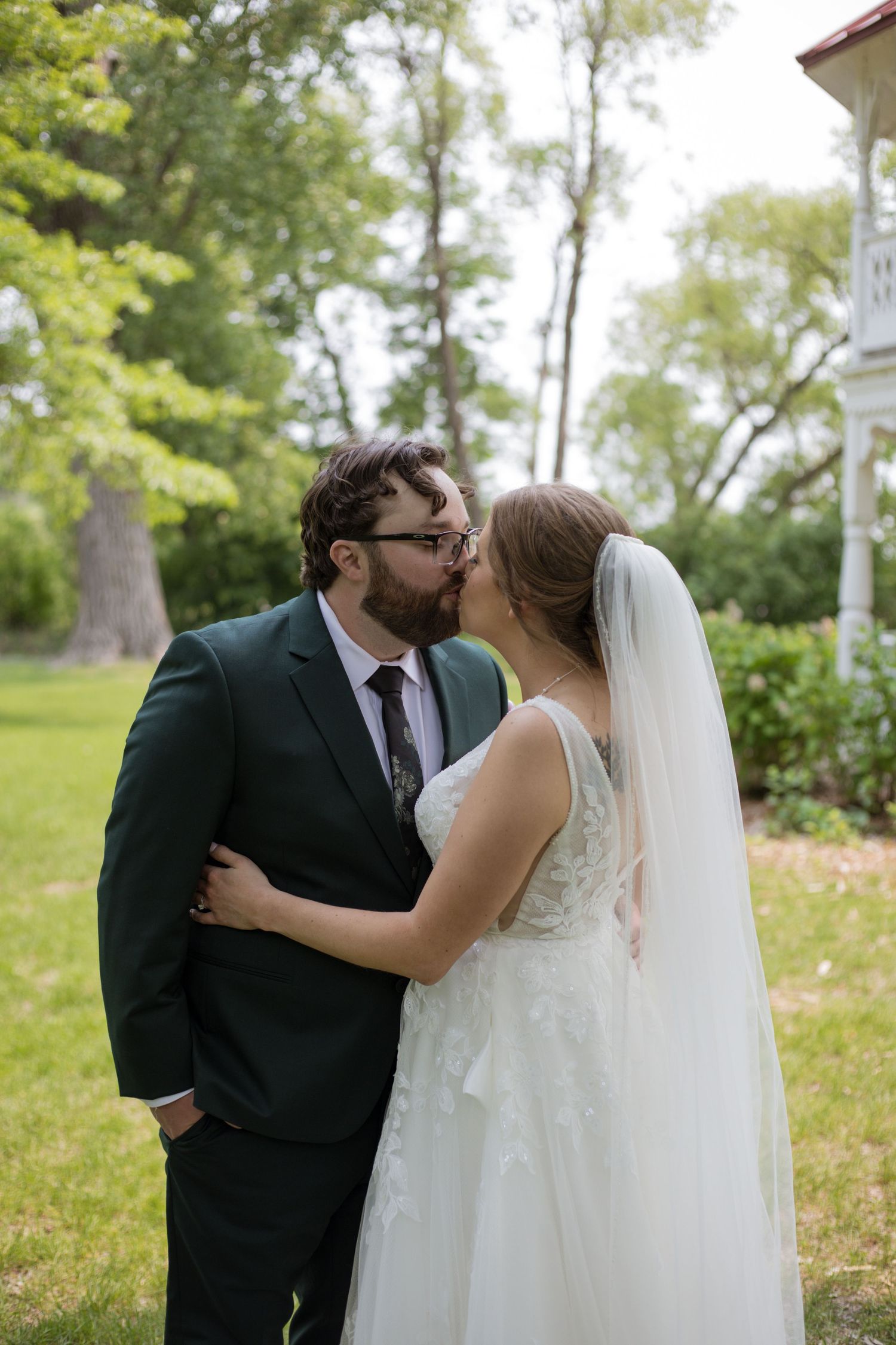 A tender wedding moment shared outdoors between newlyweds wearing a white gown and dark suit in a garden setting.