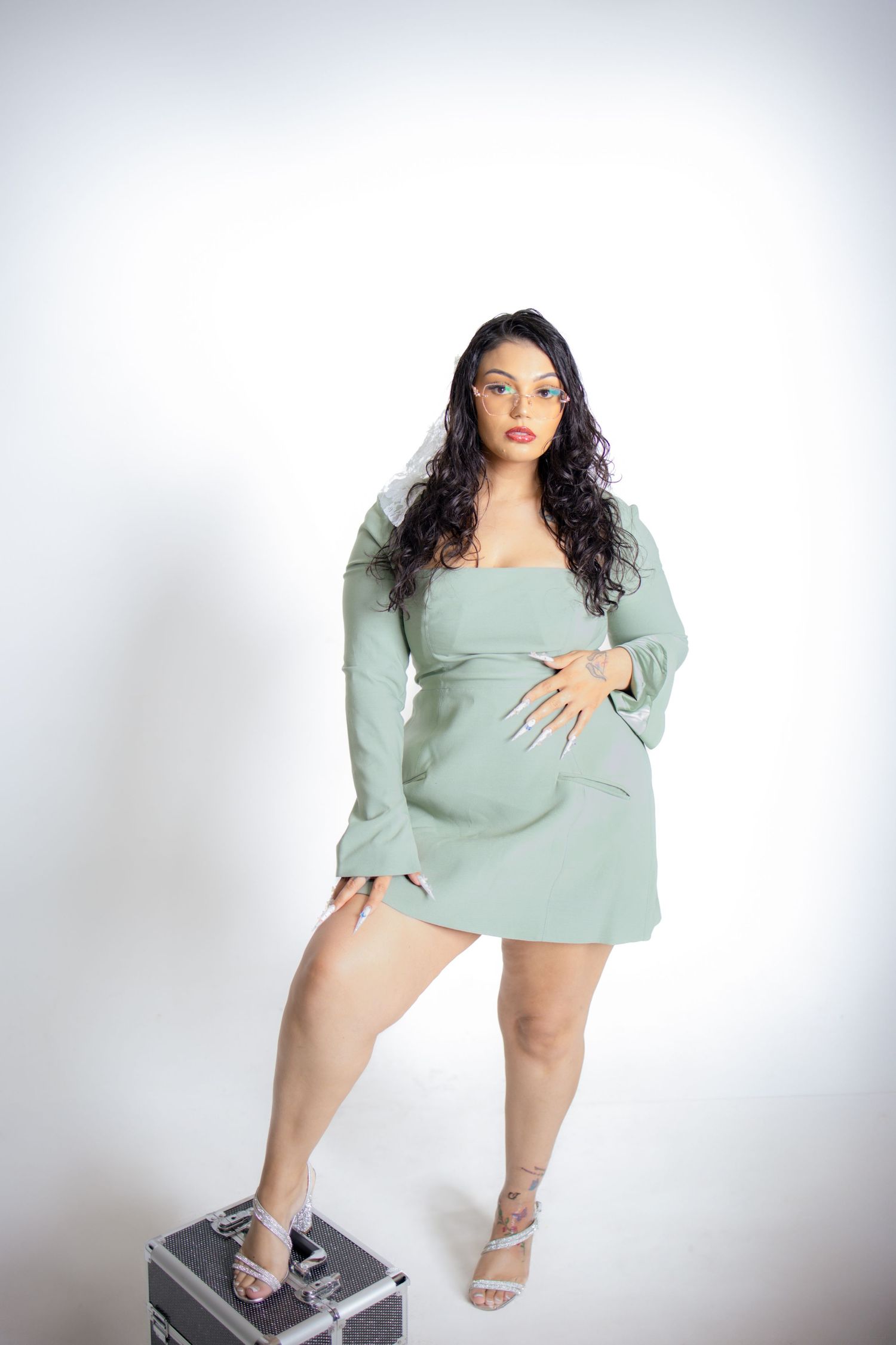 Woman in mint green dress and heels poses expressively in studio photoshoot series against white background.