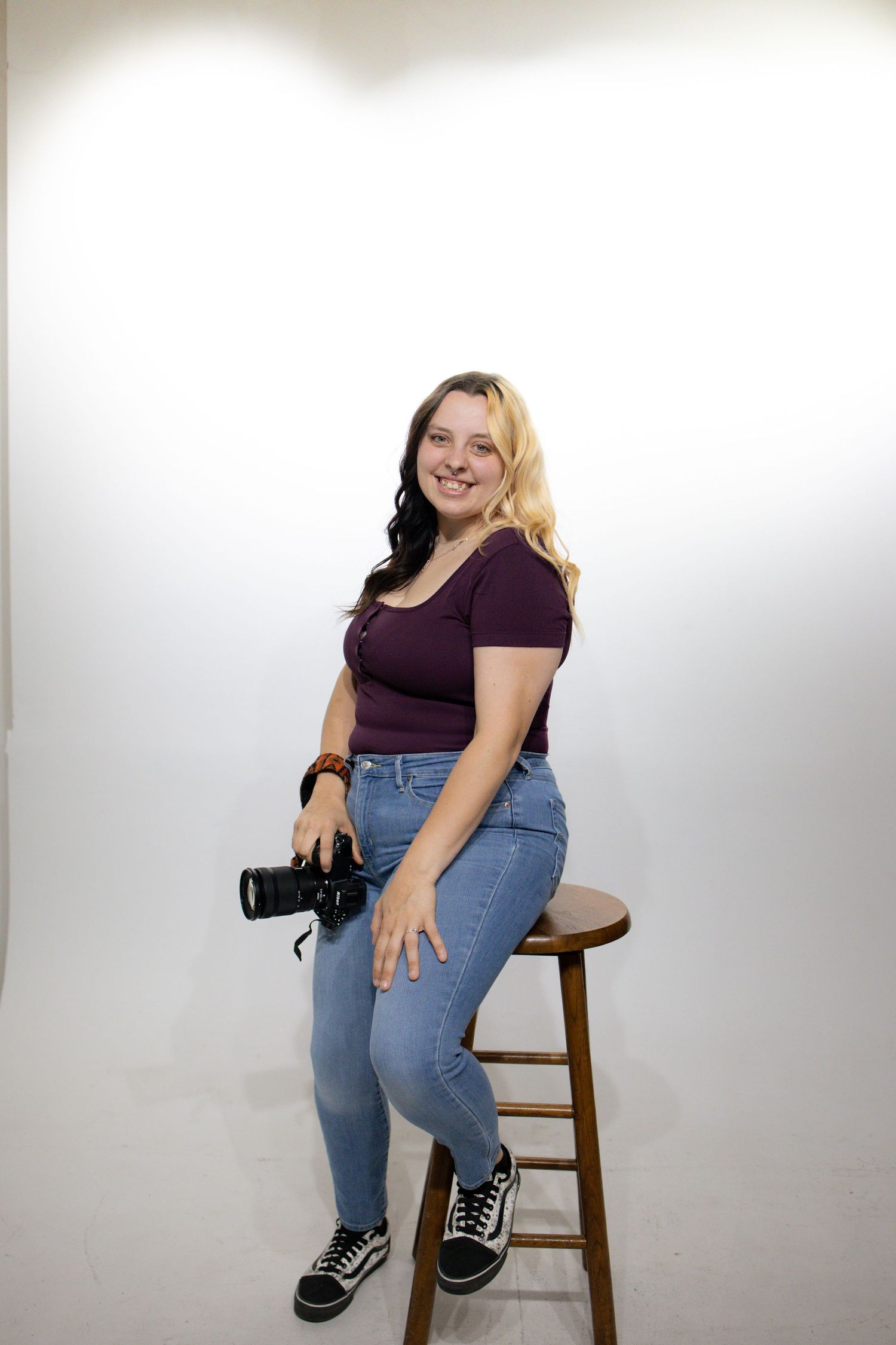 A casual photo shoot in a studio showing someone wearing blue jeans and a purple shirt while sitting on a wooden stool.