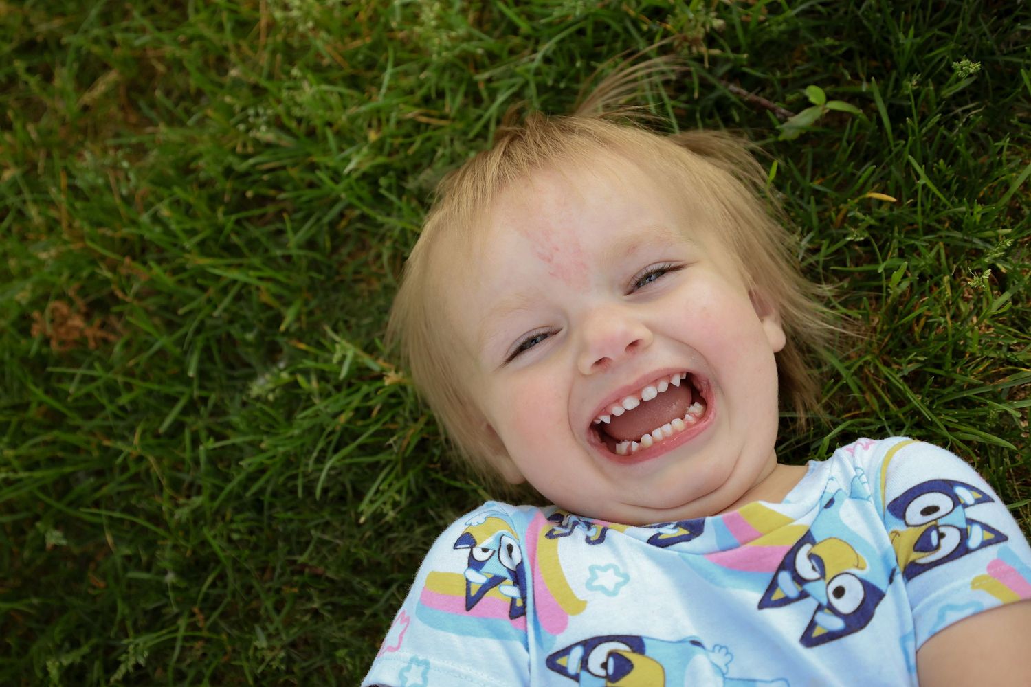 A small child lies on grass with joyful expressions in a sequence of seven connected photos showing playful moments.