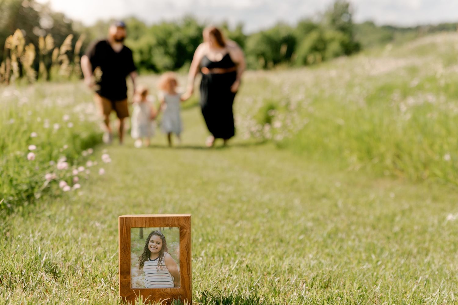 An outdoor wedding ceremony setup in a sunny field with wildflowers and wooden picture frames along the aisle.