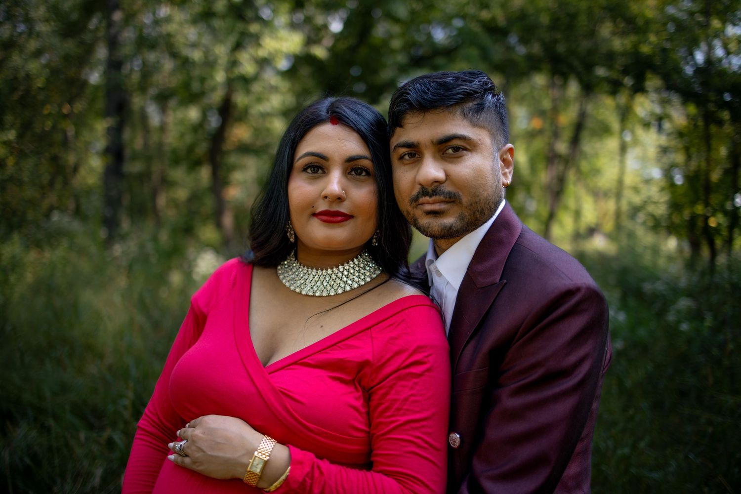 A couple in formal attire poses together outdoors in multiple romantic shots, with the woman in red and man in burgundy.