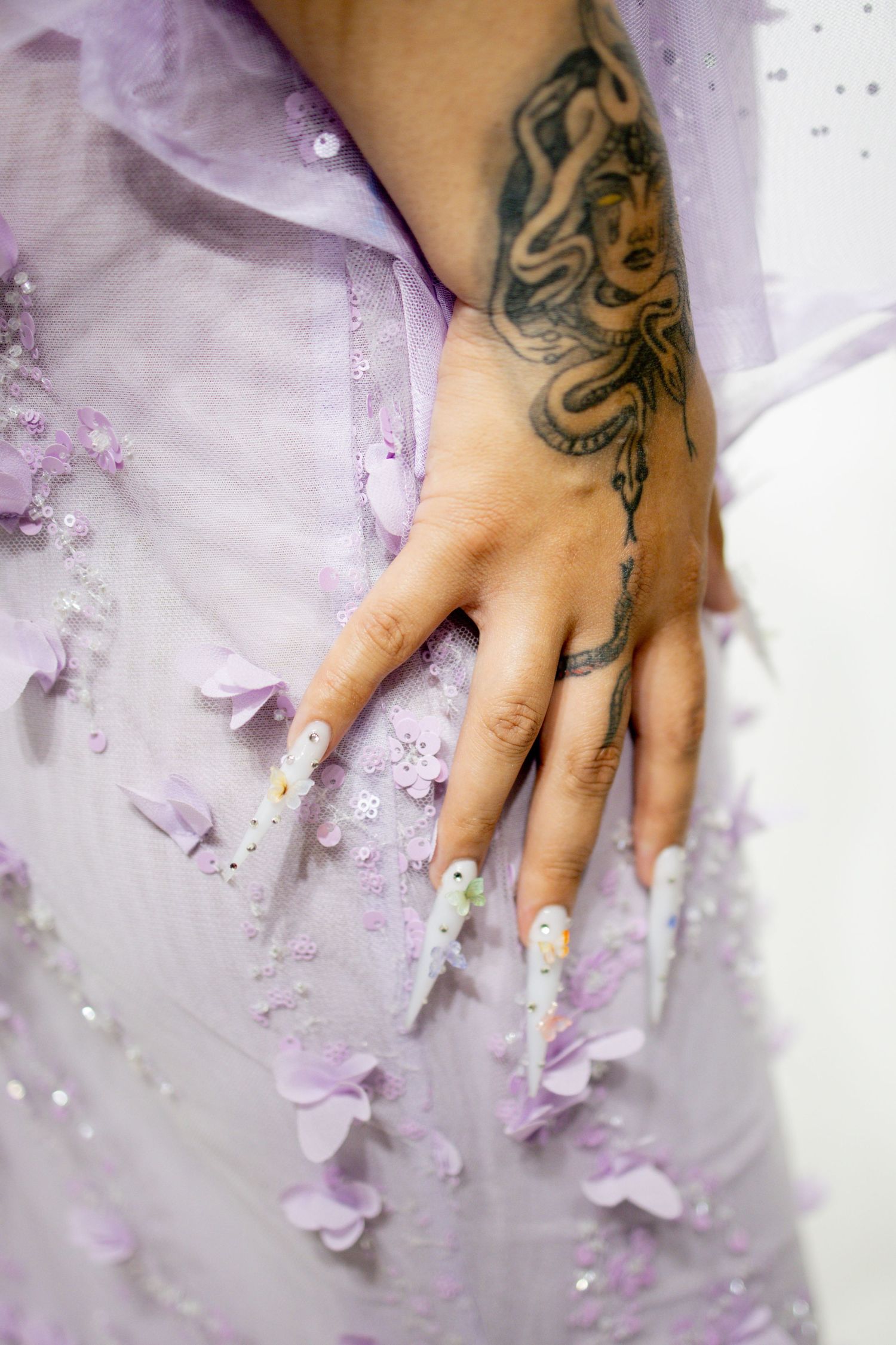 A tattooed hand rests delicately on a white surface scattered with purple flower petals and glitter.