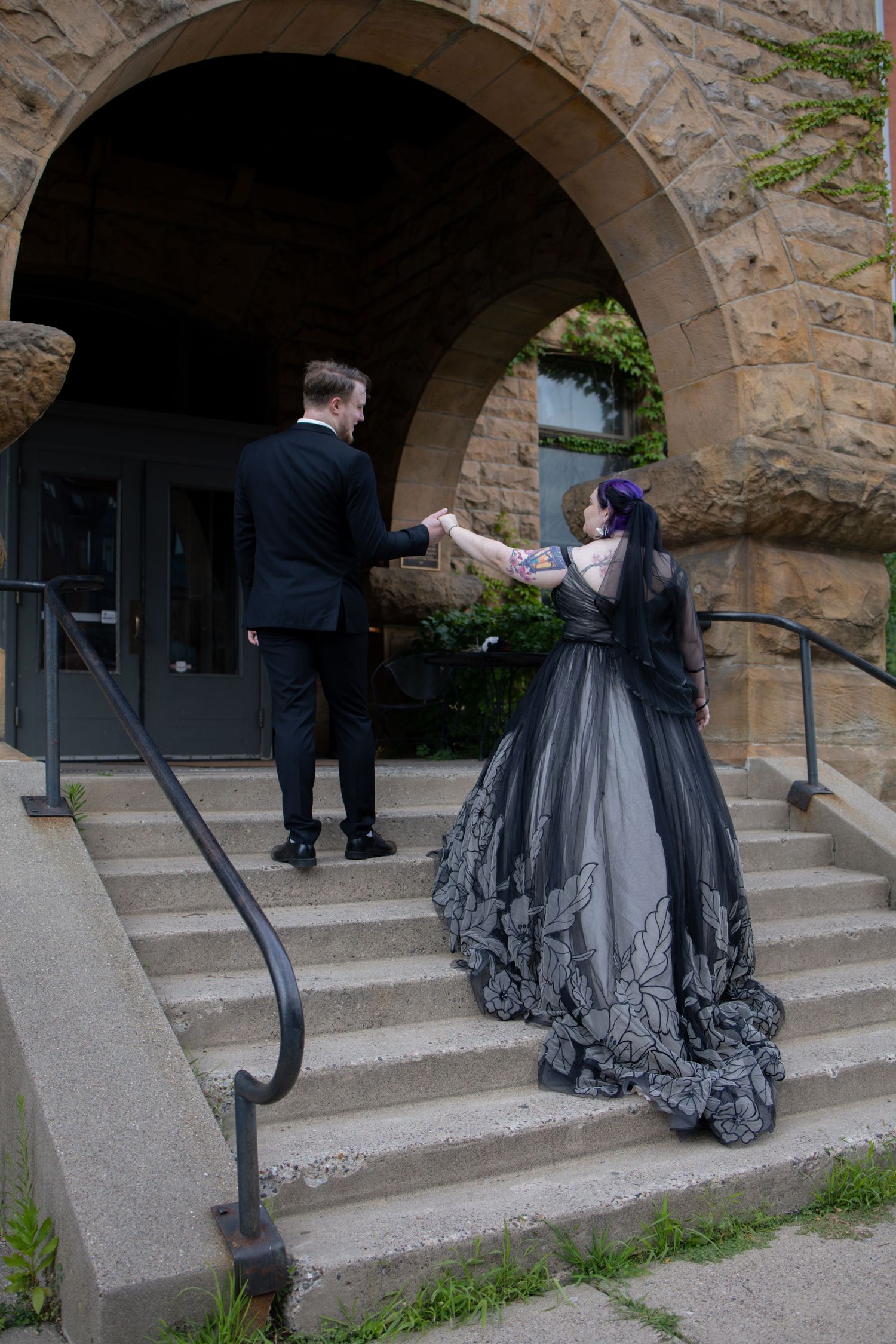 A couple poses under stone archways on concrete steps for wedding photos.