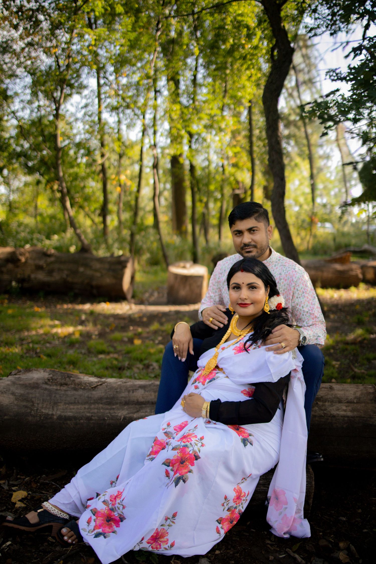 Scenic outdoor family portraits captured in a forest setting with fallen logs and sunlit trees in the background.