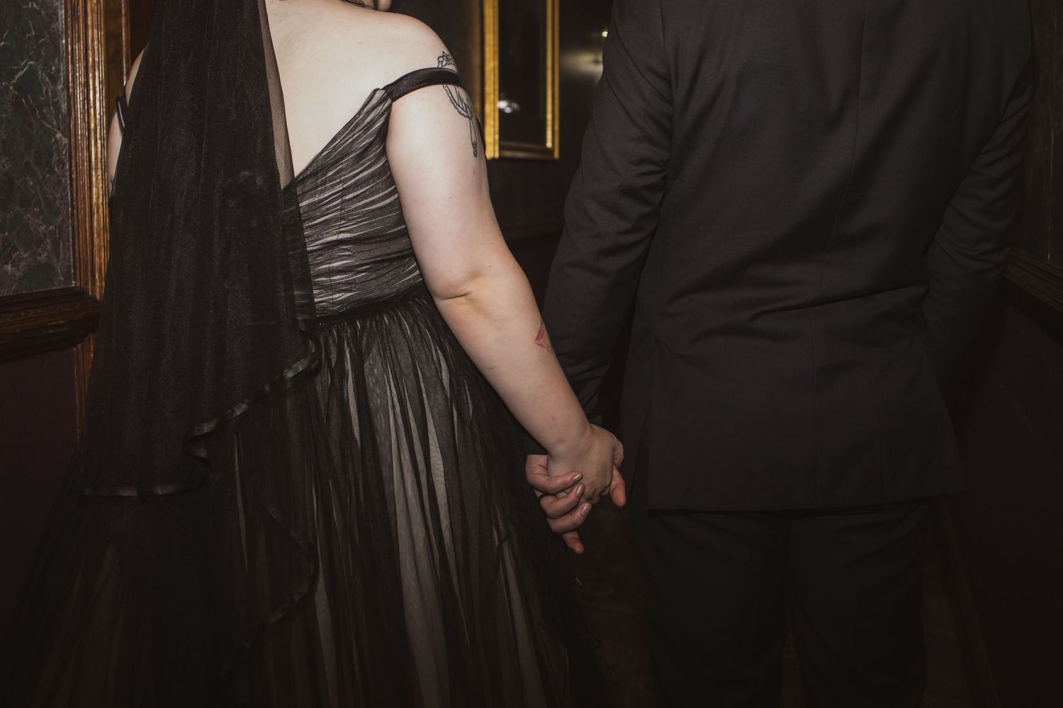 Close-up of a couple holding hands at a formal event, with the woman wearing an elegant gray off-shoulder gown.