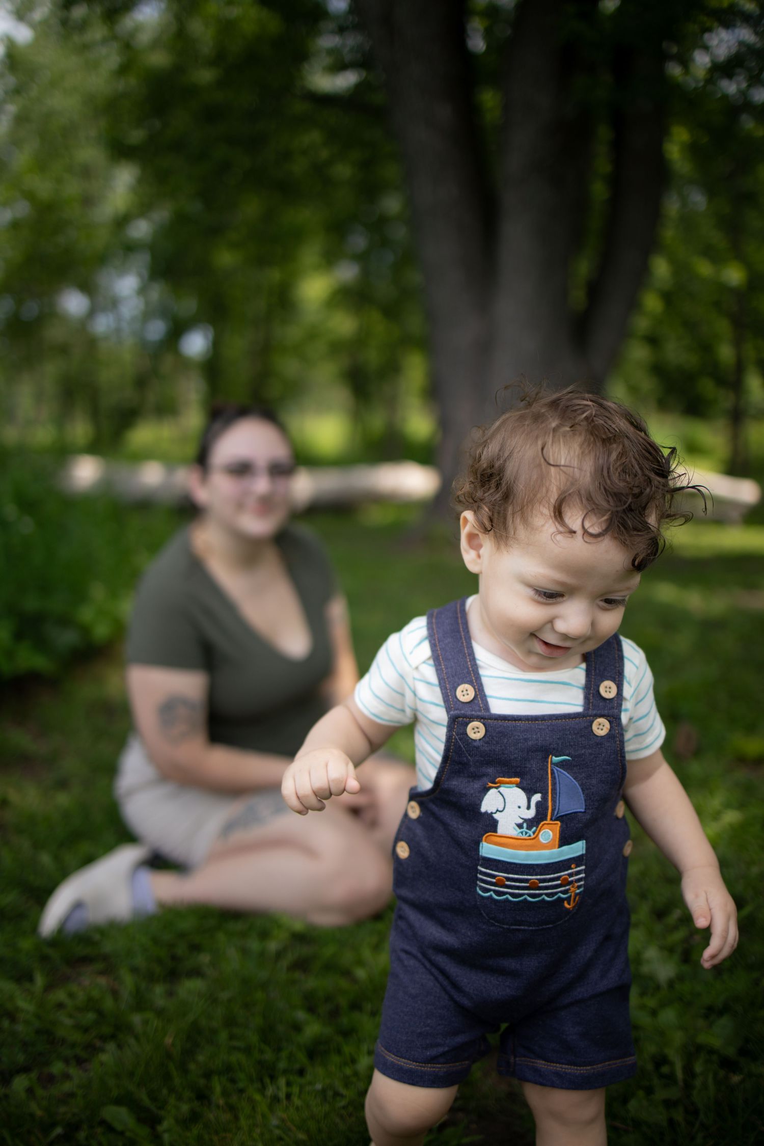 Small child in denim overalls playing outdoors in a garden setting with lush greenery in the background.