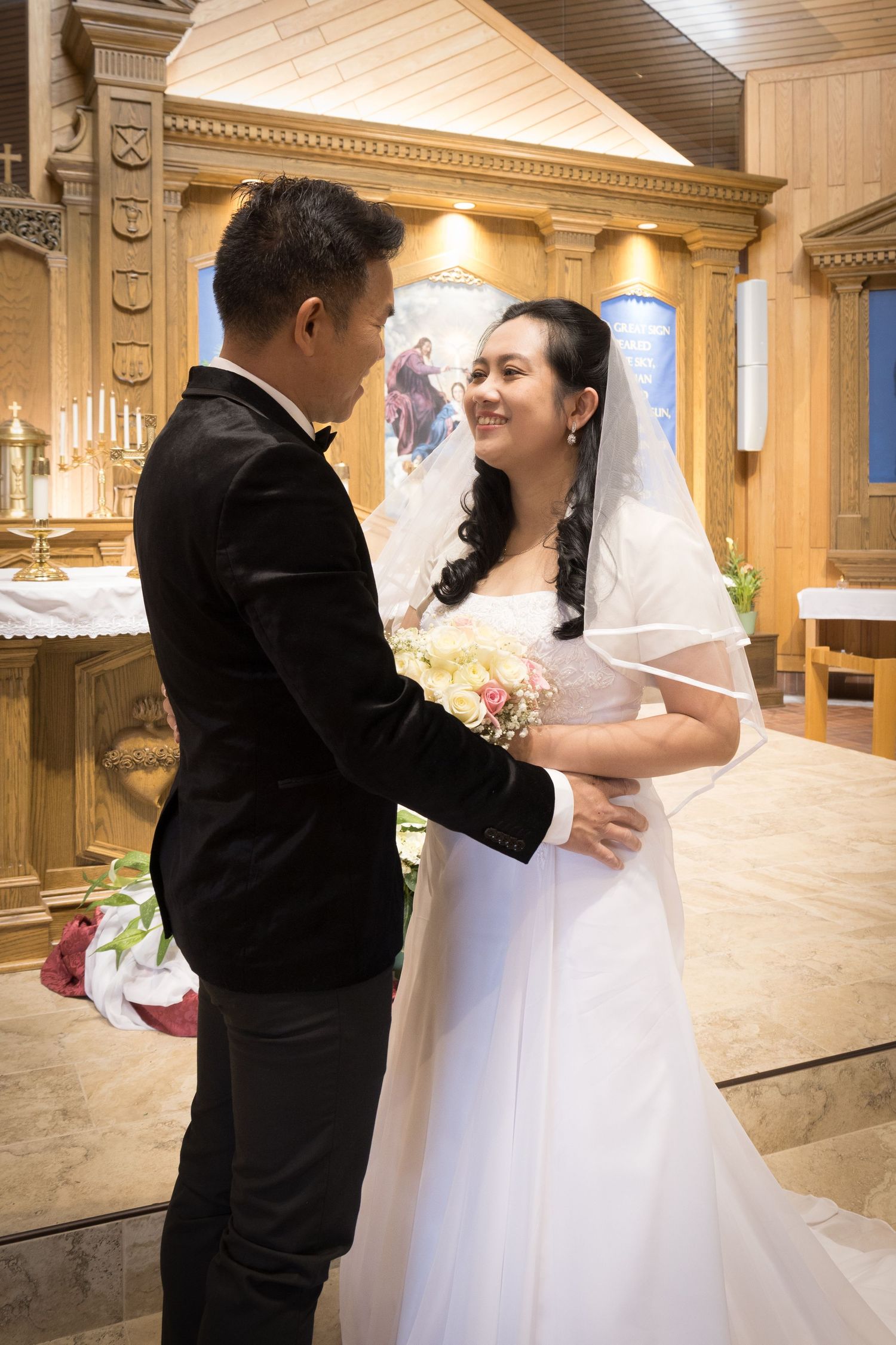 A couple in formal wedding attire share an intimate moment at the altar in an elegant church setting.