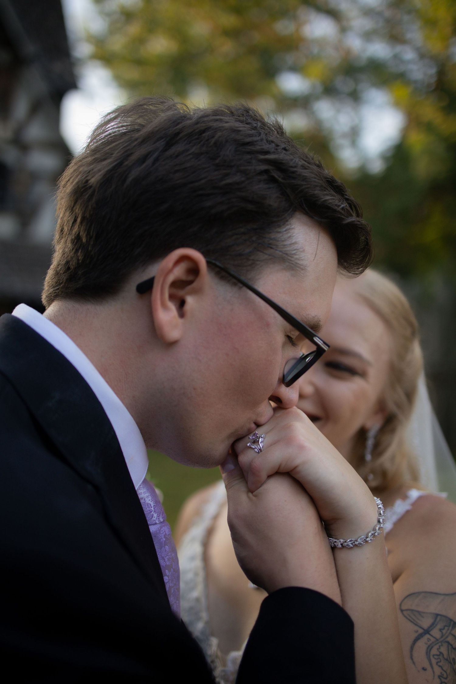 A tender moment between newlyweds as the groom kisses the bride's hand during an outdoor wedding ceremony.