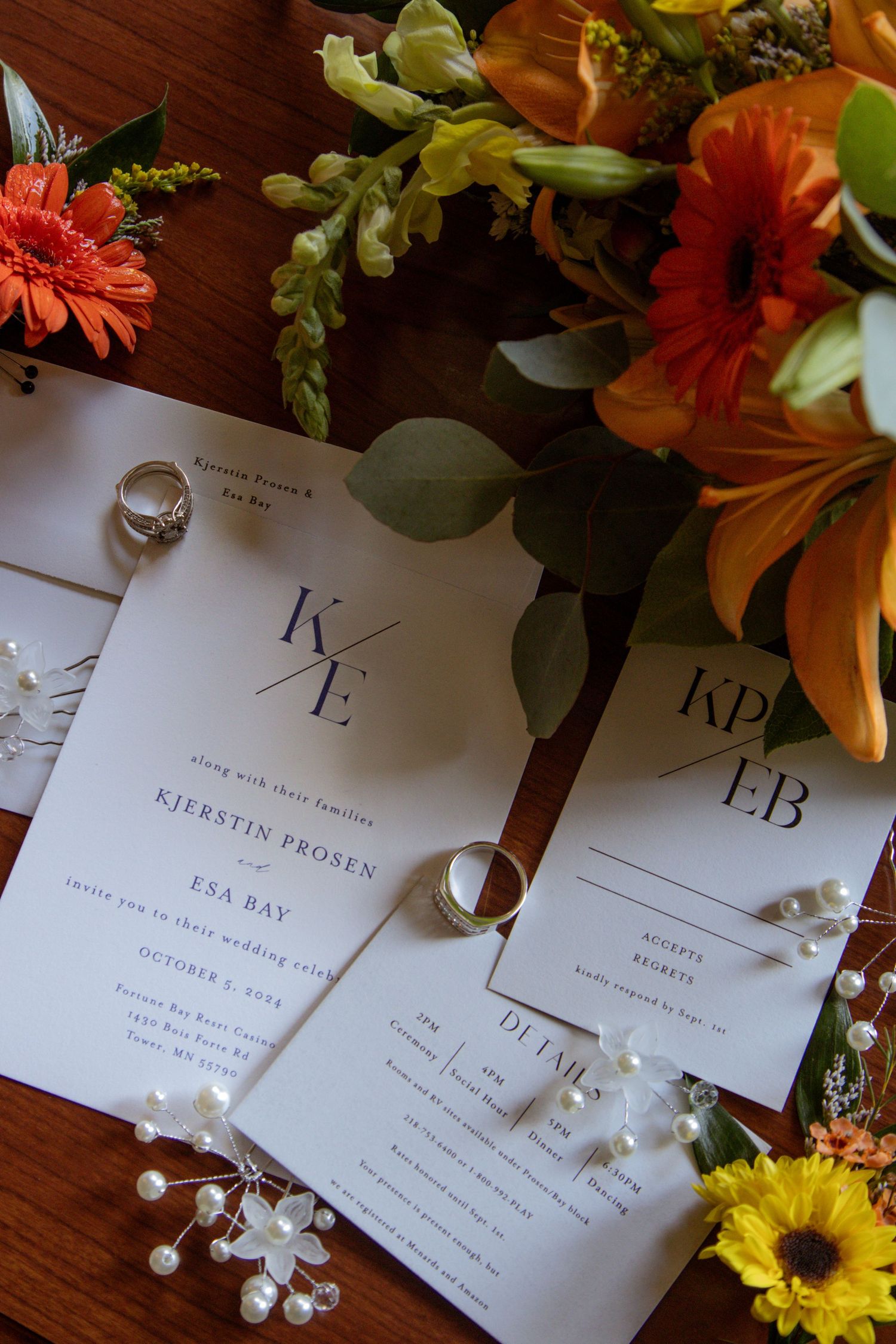 Elegant wedding invitations with floral arrangements featuring orange and yellow flowers on a dark wooden surface.