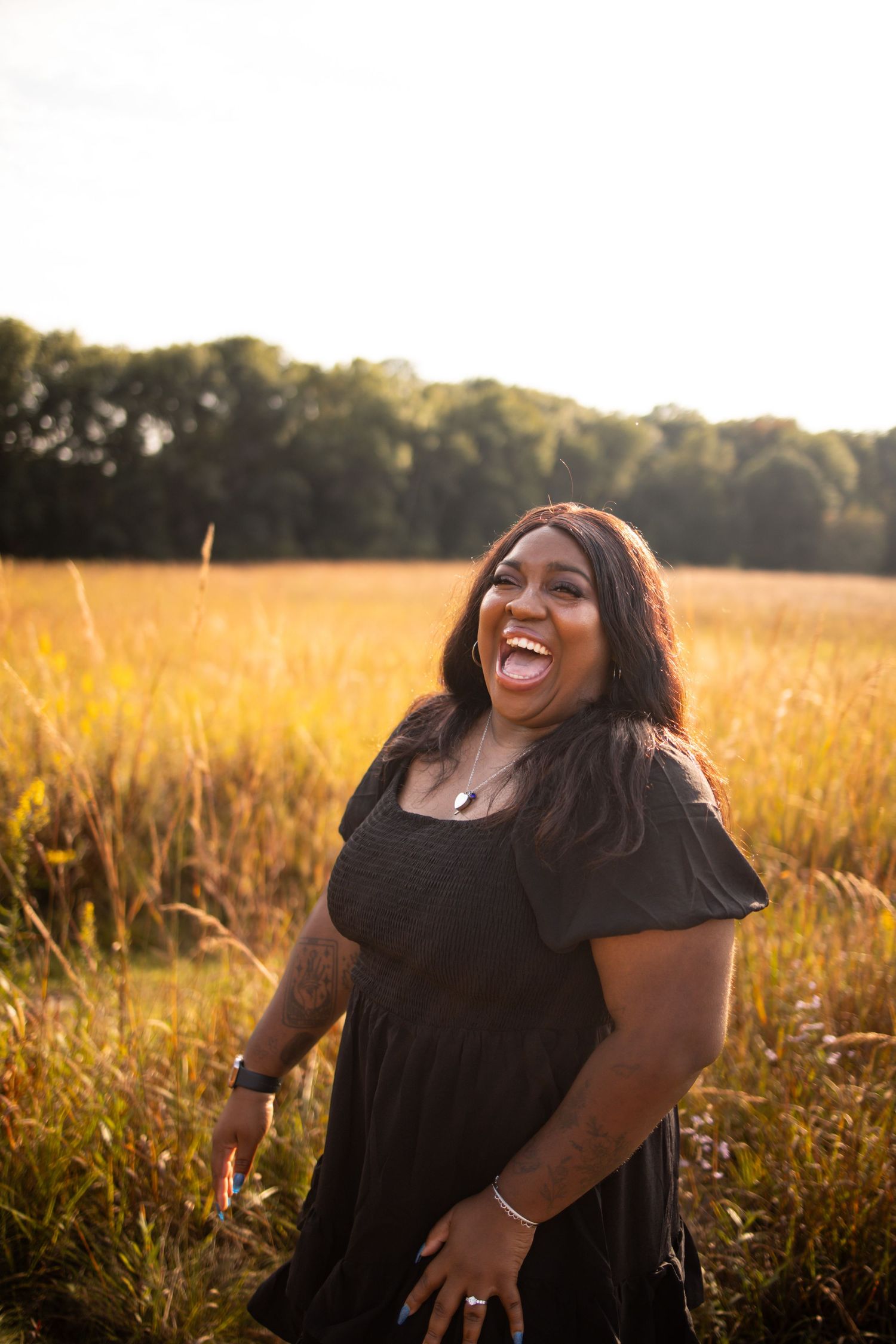 A joyful silhouette laughs in a golden wheat field during sunset, wearing a black dress with puff sleeves.