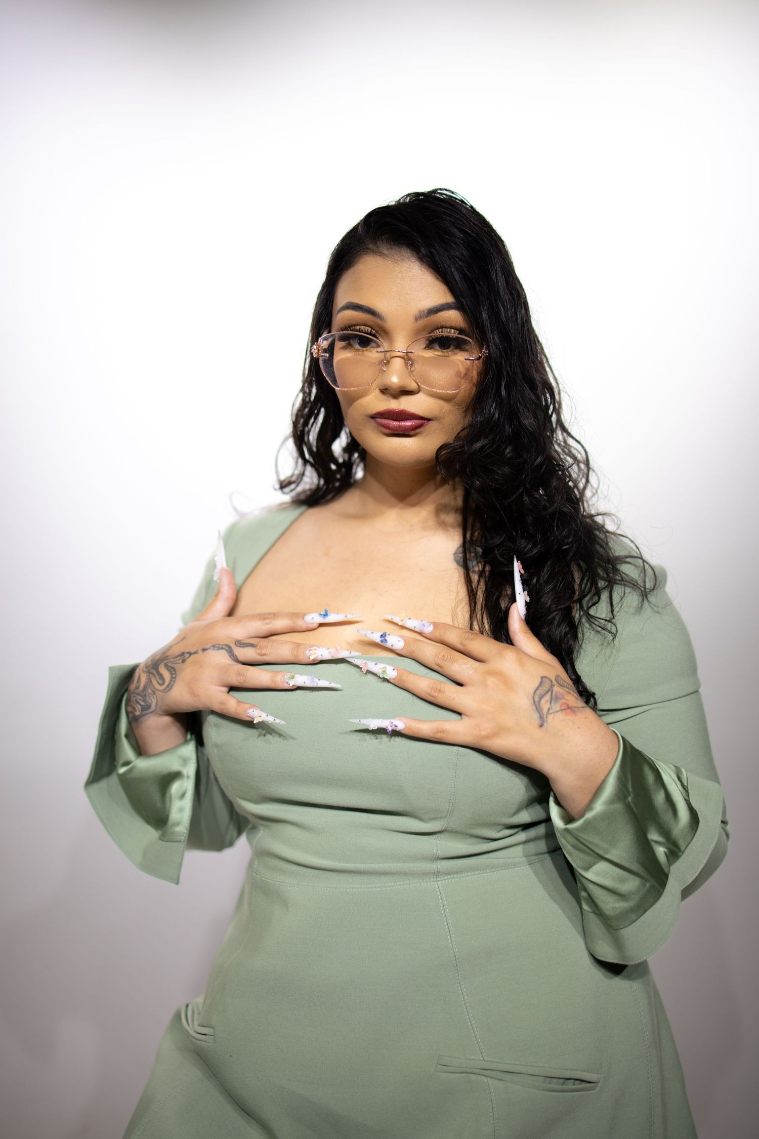 Portrait of someone wearing a mint green dress with long sleeves and glasses, posing against a light background.