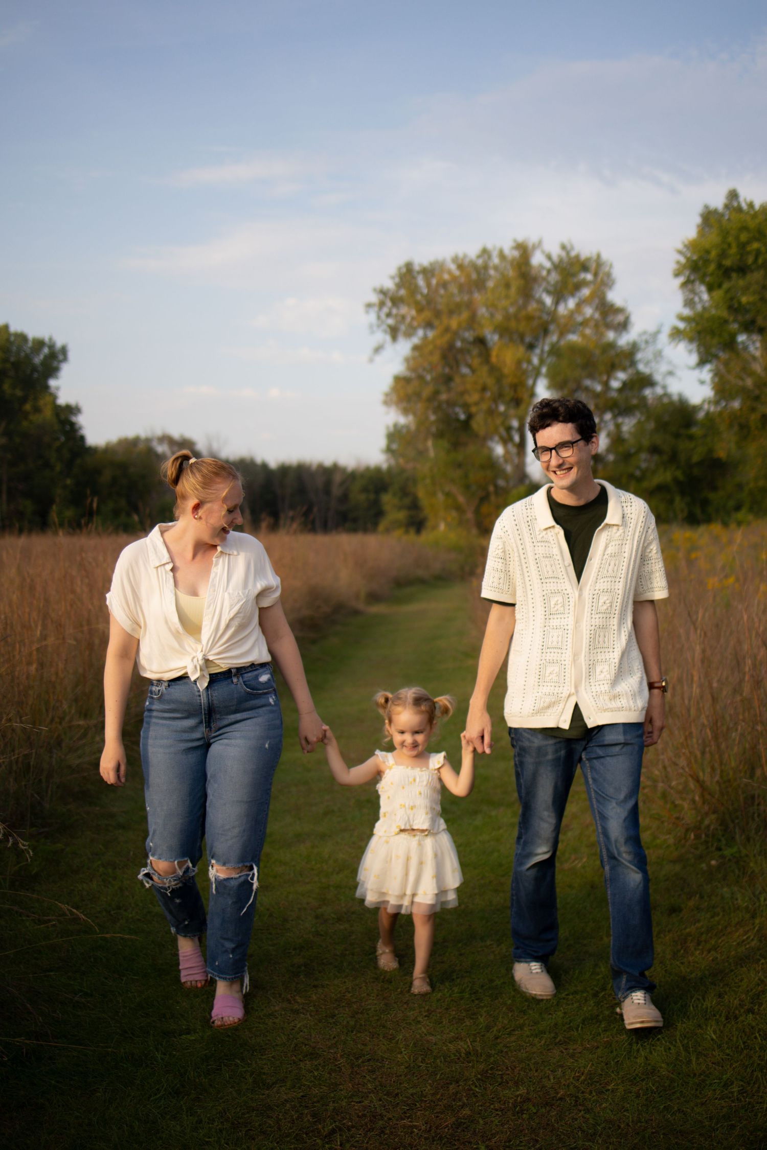 Family walking together hand in hand on a grass path through tall autumn grasses during golden hour.
