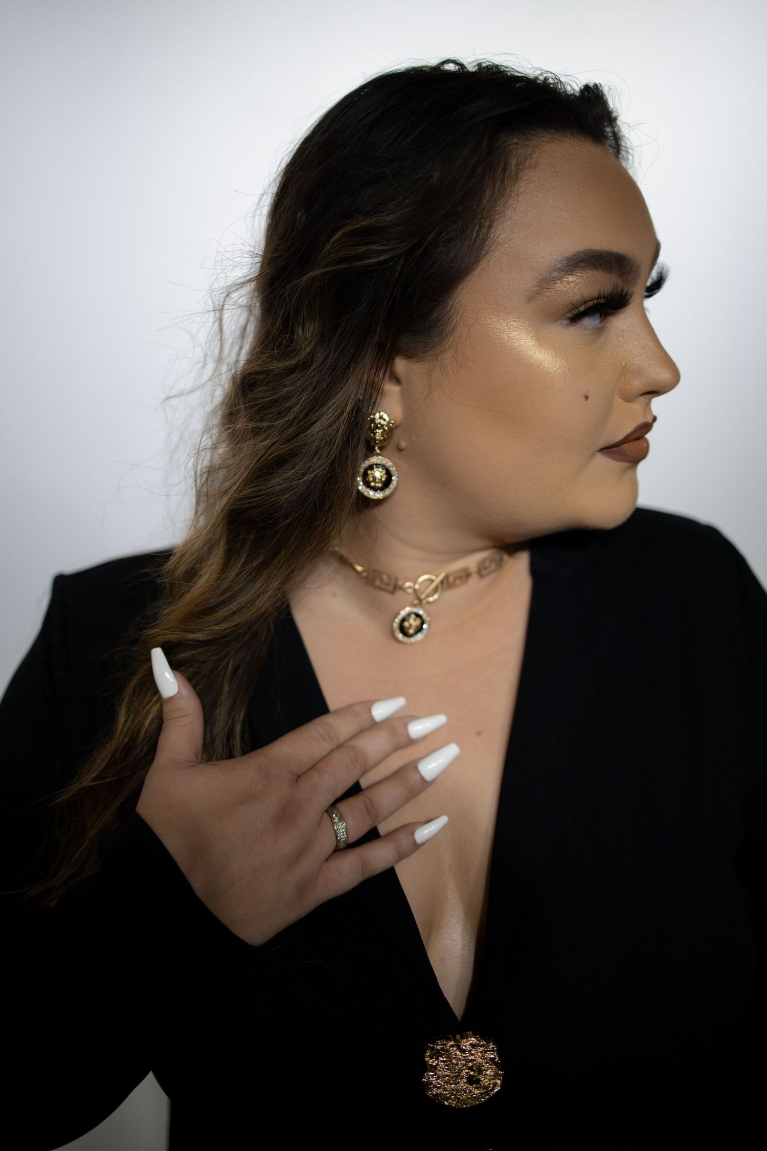 Side profile portrait showcasing elegant jewelry and makeup with dramatic lighting against white backdrop.