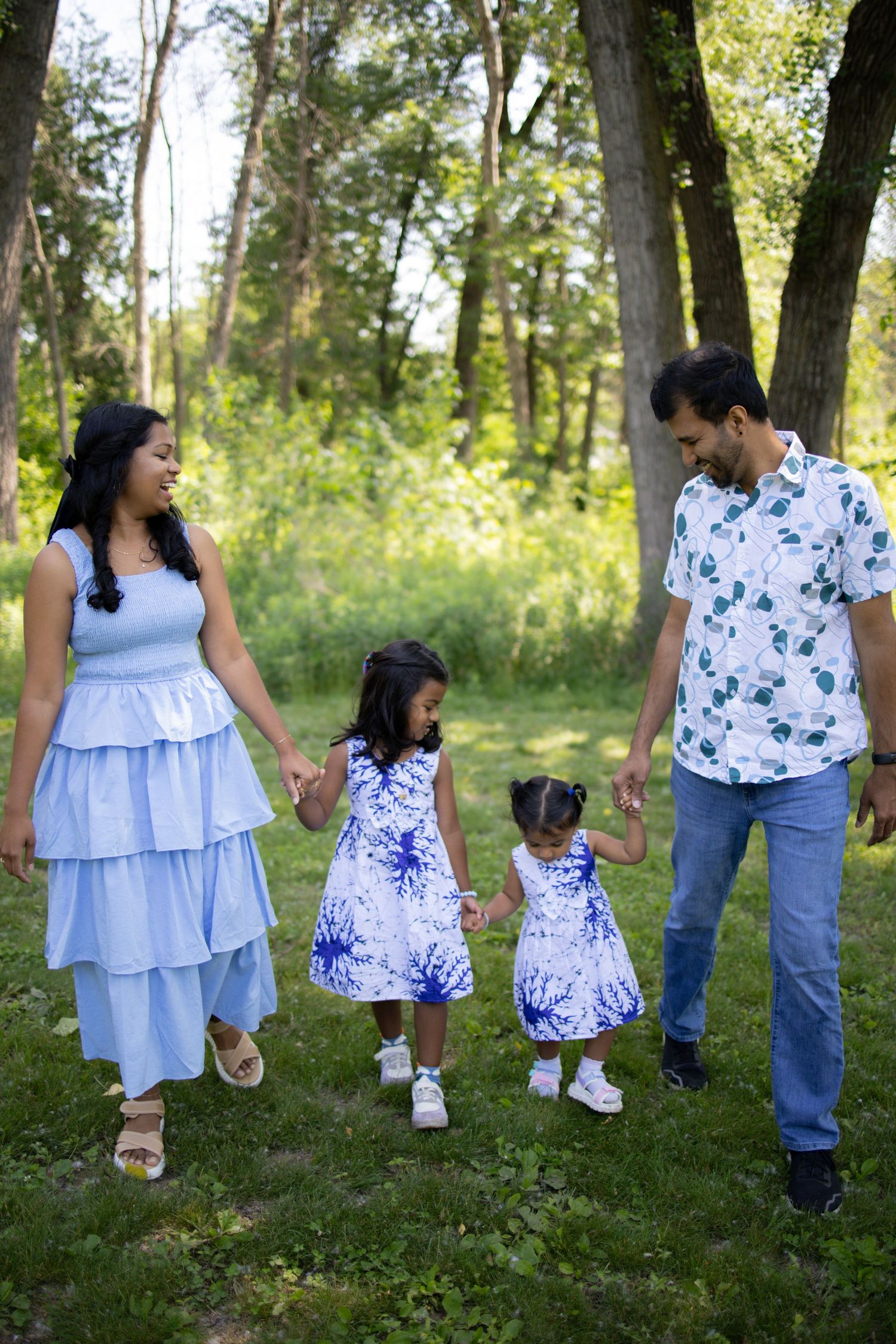 A family group wearing coordinated white and blue outfits walks together in a park setting with green trees and grass.