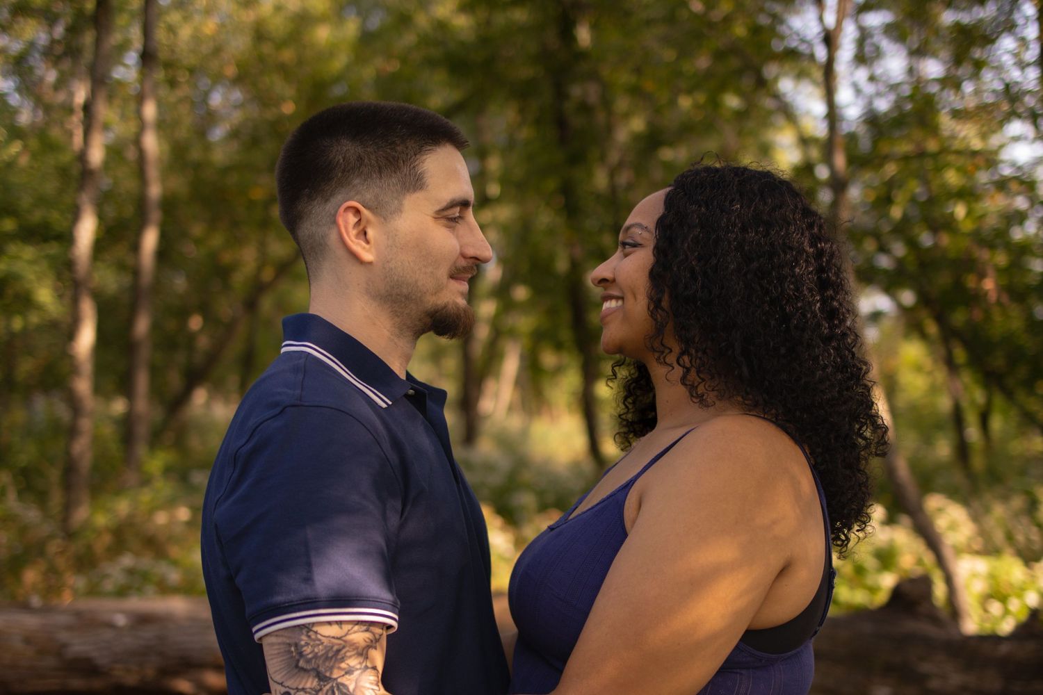 A couple shares an intimate moment together during a golden hour photoshoot in a sunlit wooded setting.