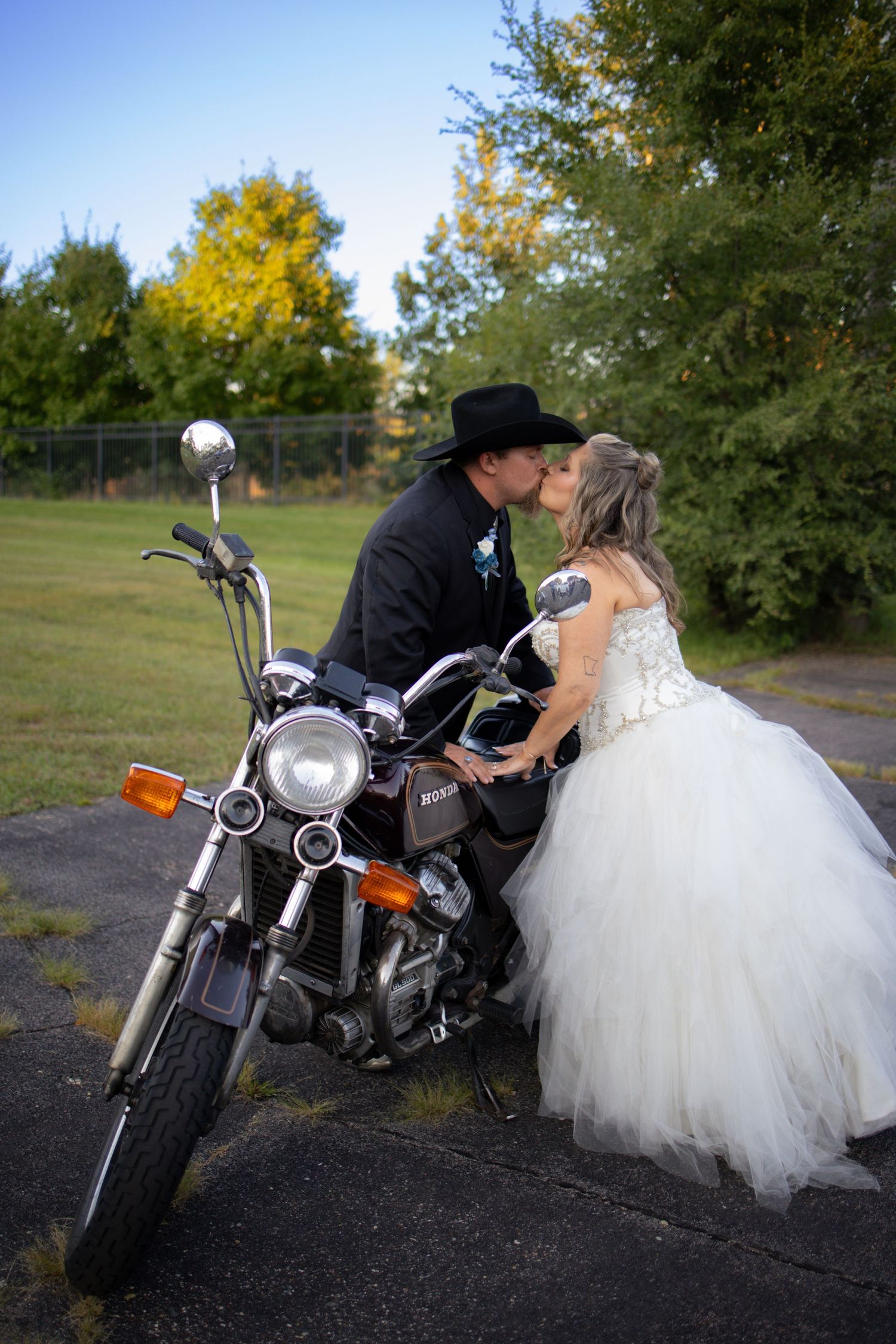 A motorcycle with a couple in wedding attire creates a romantic series of poses in an outdoor setting.