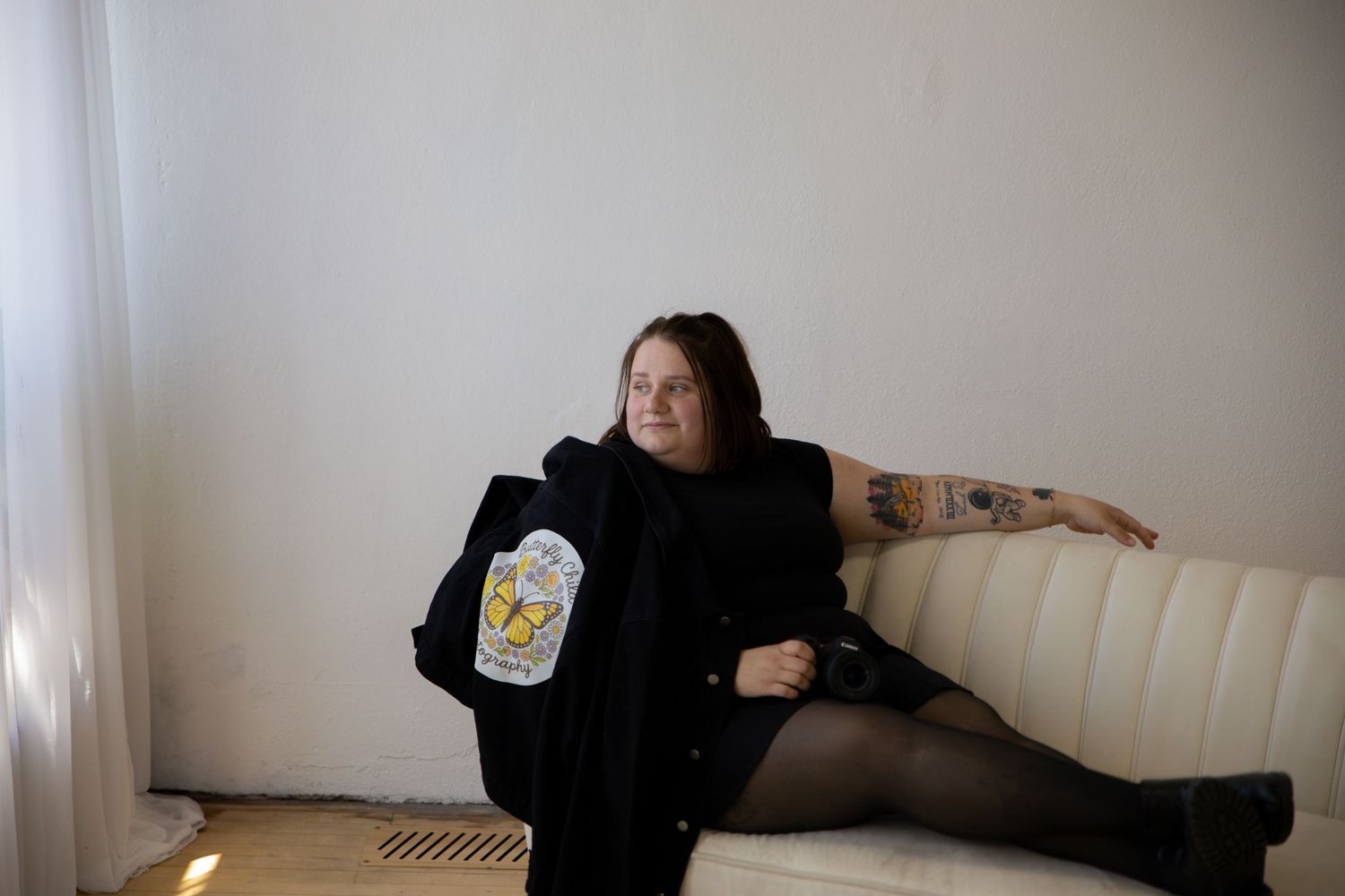 Person in black outfit lounging casually on white furniture in a minimalist room interior.