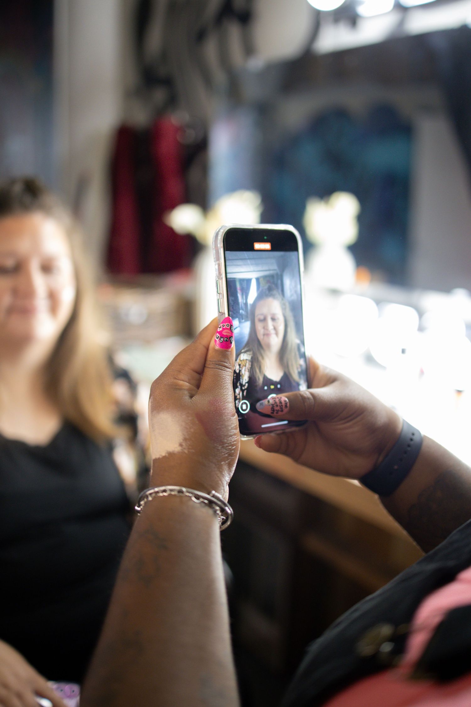 Someone takes a photo with an iPhone camera, showing painted fingernails and a silver bracelet in focus.