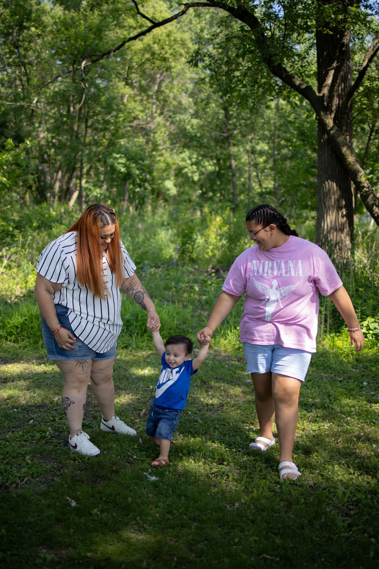 People enjoy a summer stroll together while holding hands along a shaded path in a lush green park.