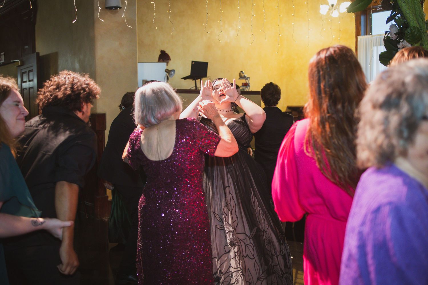 A crowded dance floor filled with people dancing together under warm lighting in a party setting.