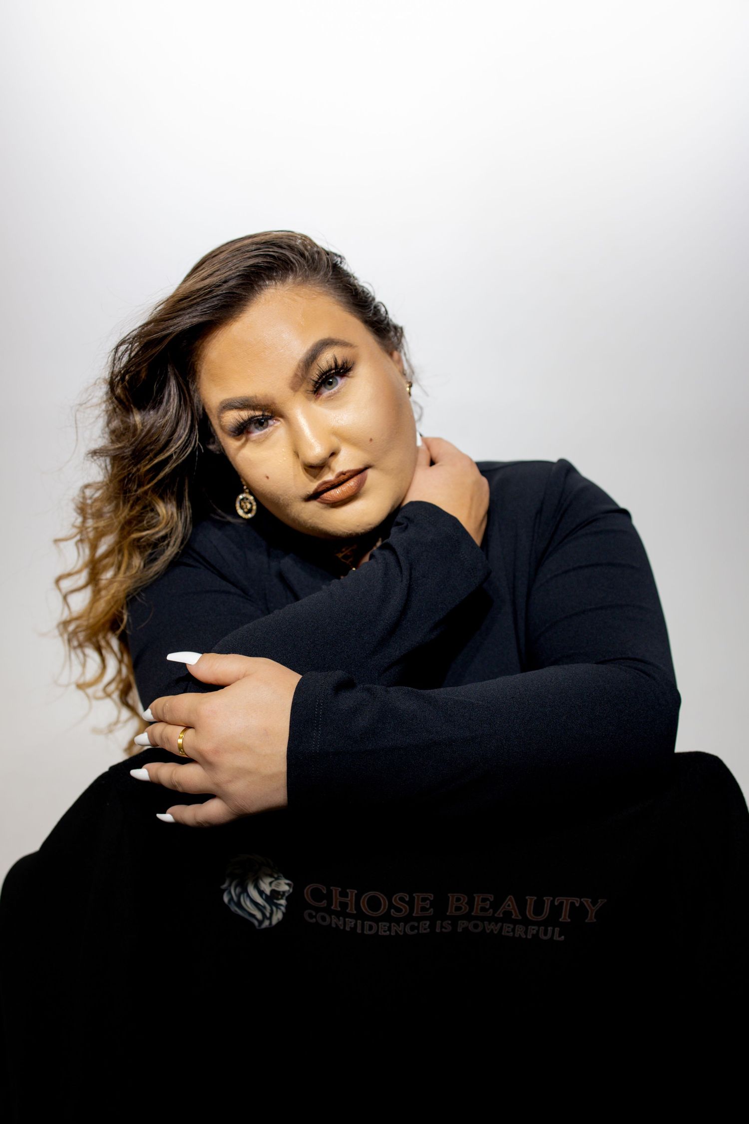 Person in black sweater poses against white background with dramatic lighting and flowing hair.