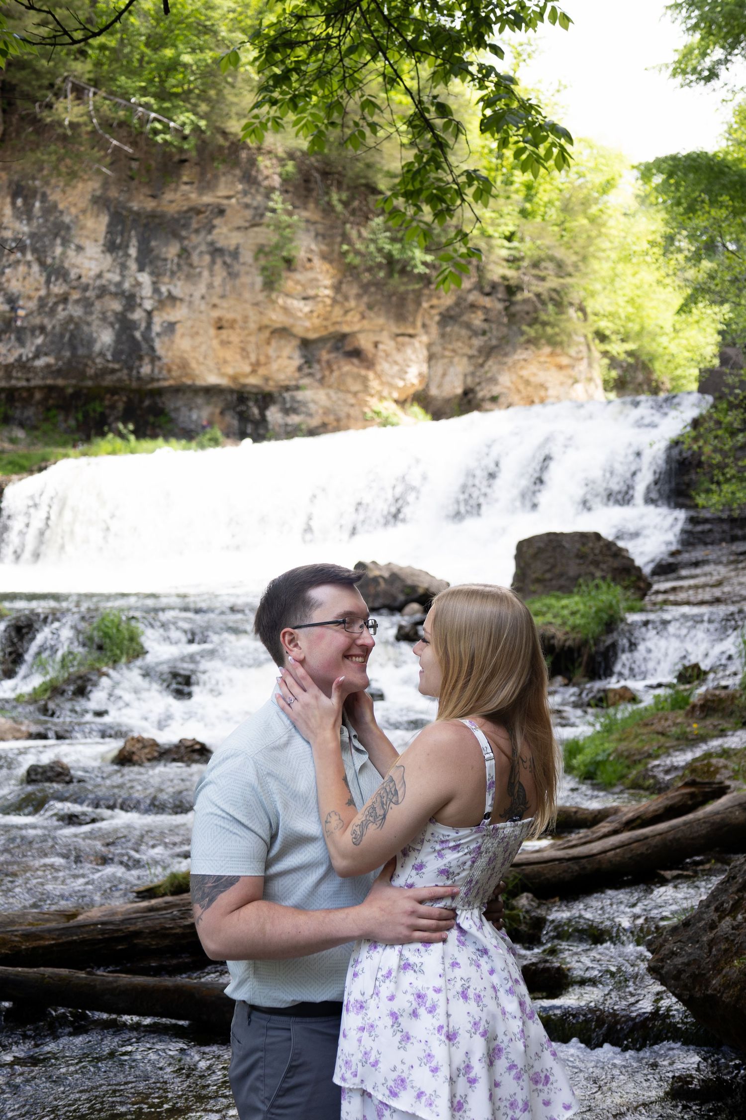 A couple shares romantic moments by a cascading waterfall in a scenic natural setting.