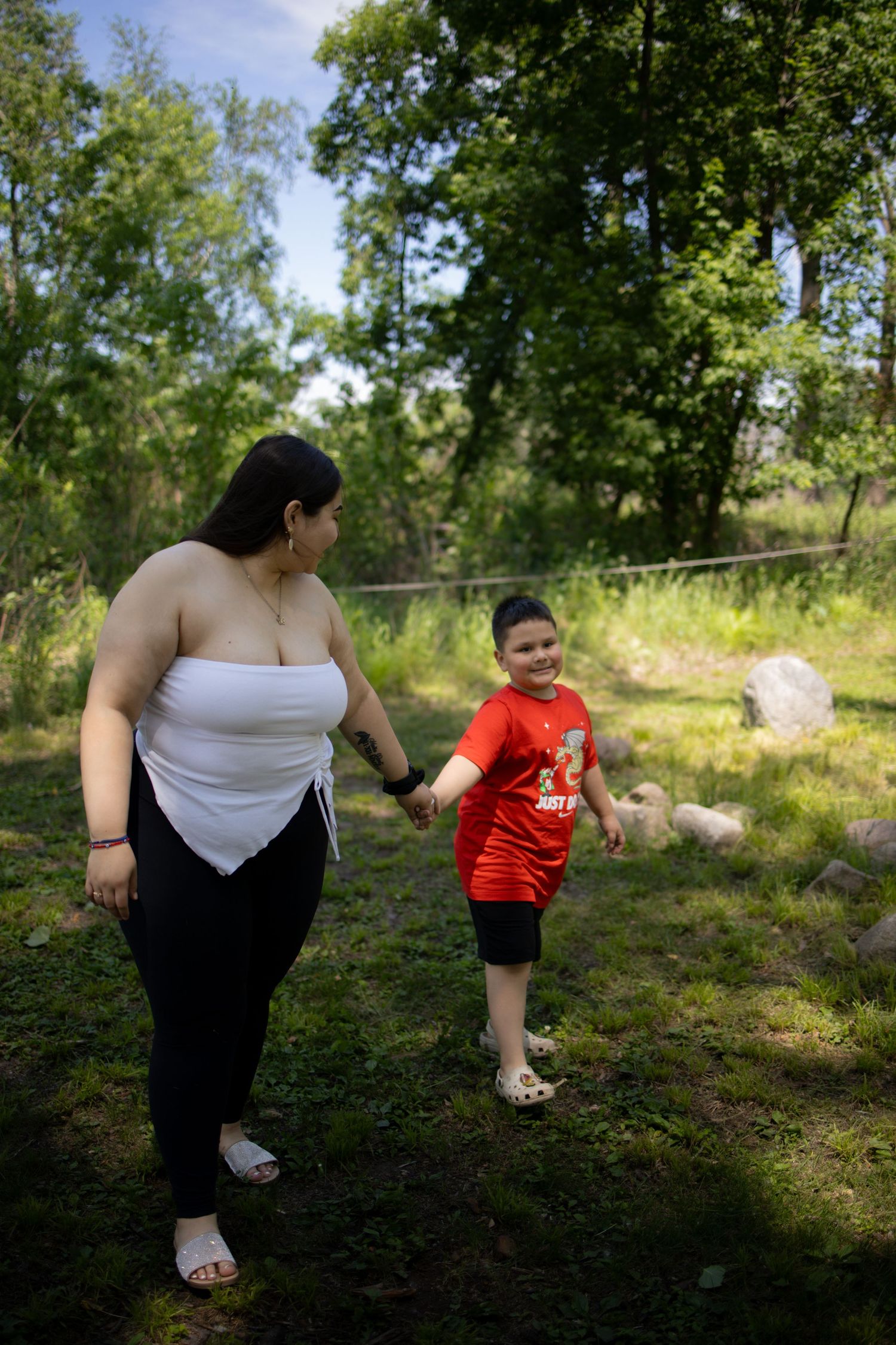 Walking together in a sunny forest clearing on a summer day, one in a red shirt and the other in white.