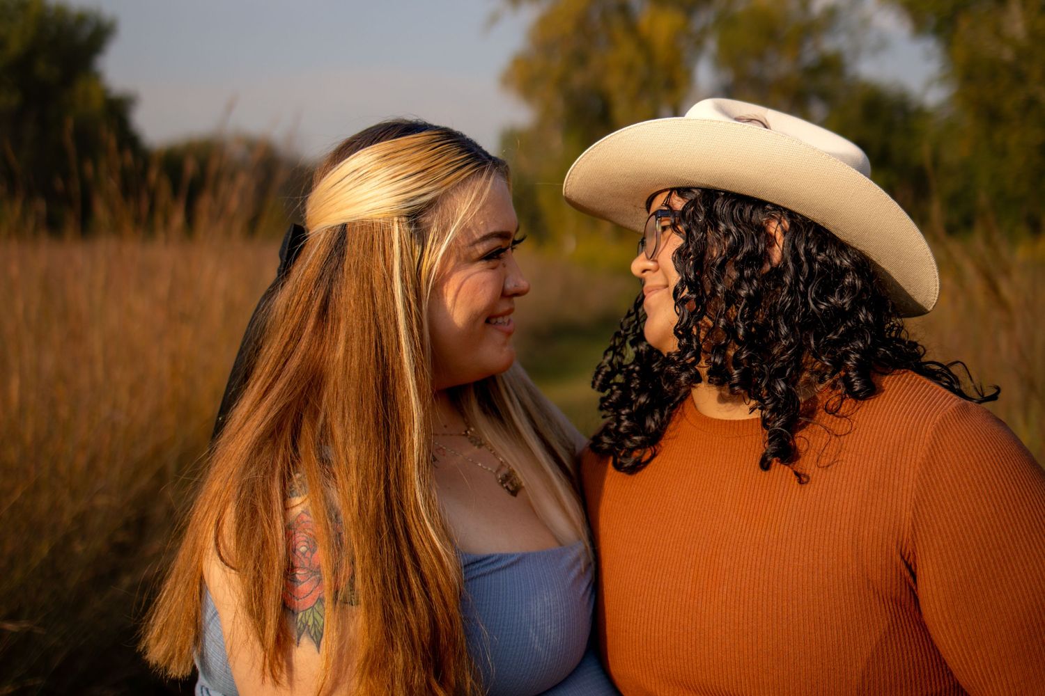 A couple shares an intimate moment outdoors in golden light, one wearing a cowboy hat and rust-colored sweater.