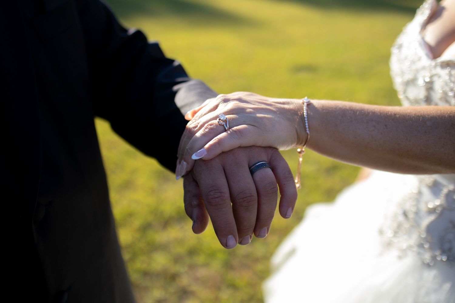 Close-up of hands exchanging wedding rings during an outdoor ceremony with soft sunlight in the background.