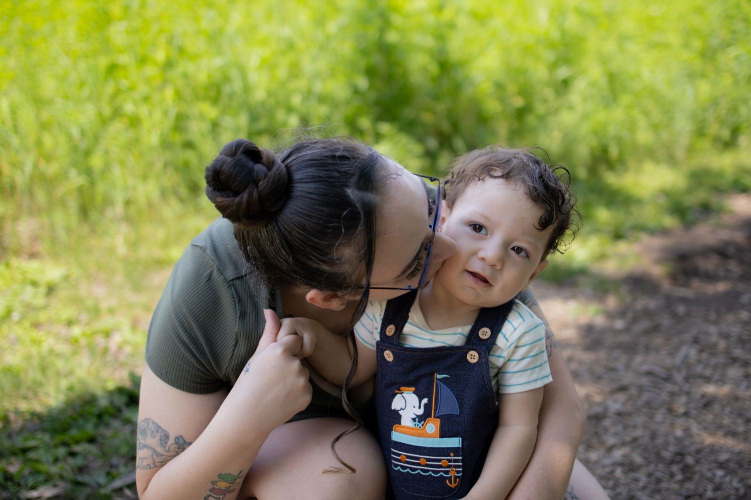 Two people share a tender moment while sitting together on a path outdoors with green foliage in the background.