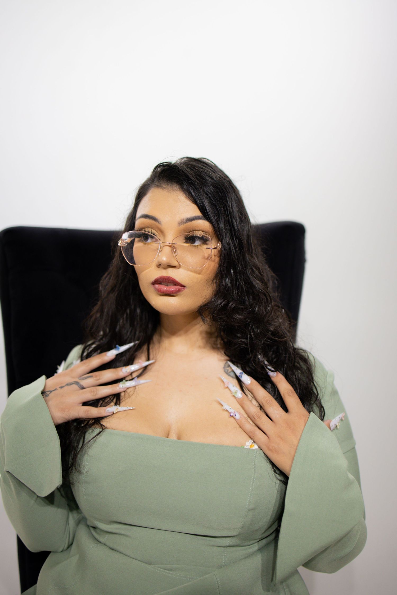 Four artistic portrait poses in a studio showing a curvy figure in sage green attire with dramatic makeup and flowing hair.