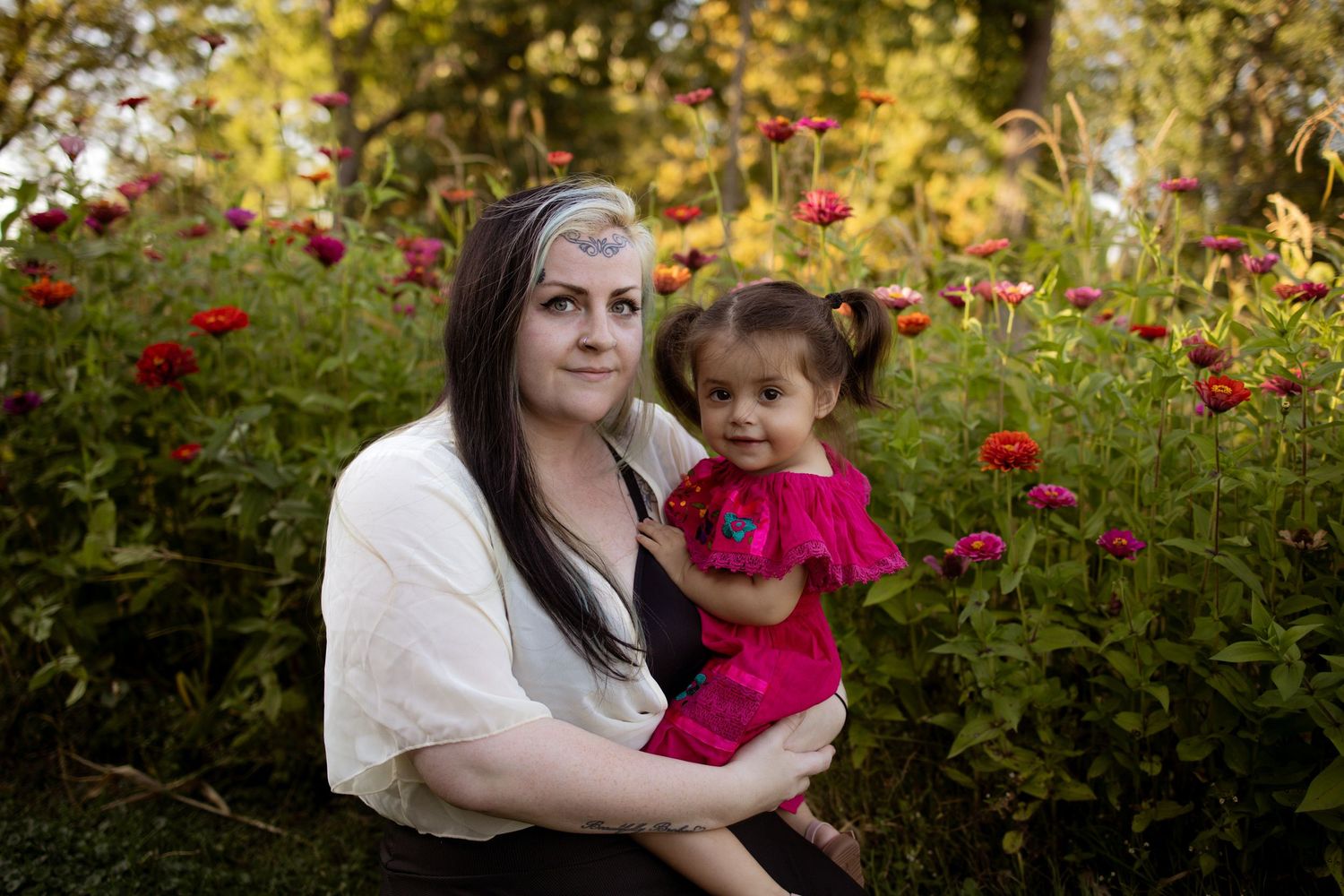 A mother and child share tender moments together in a garden with blooming red roses during a fall photo session.