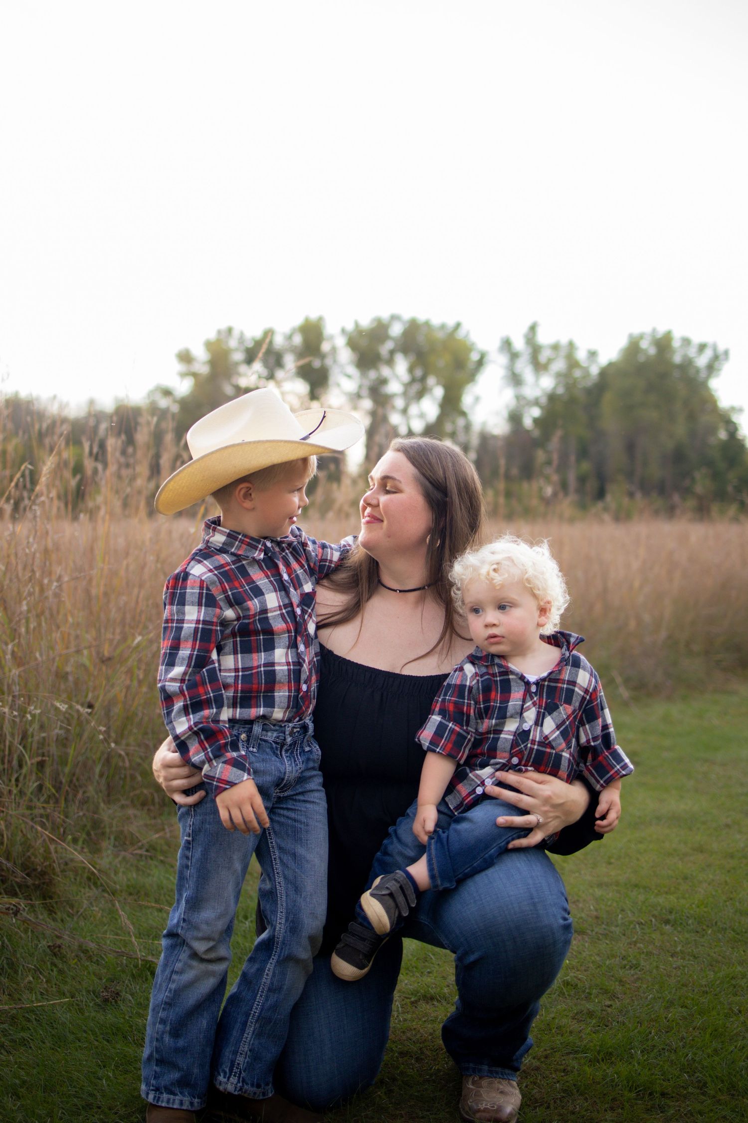 A family in matching plaid and denim outfits shares tender moments together in a grassy field at sunset.